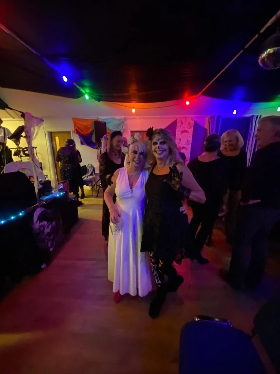 People dressed in costumes celebrating at a party with colorful lights, some wearing Halloween makeup.