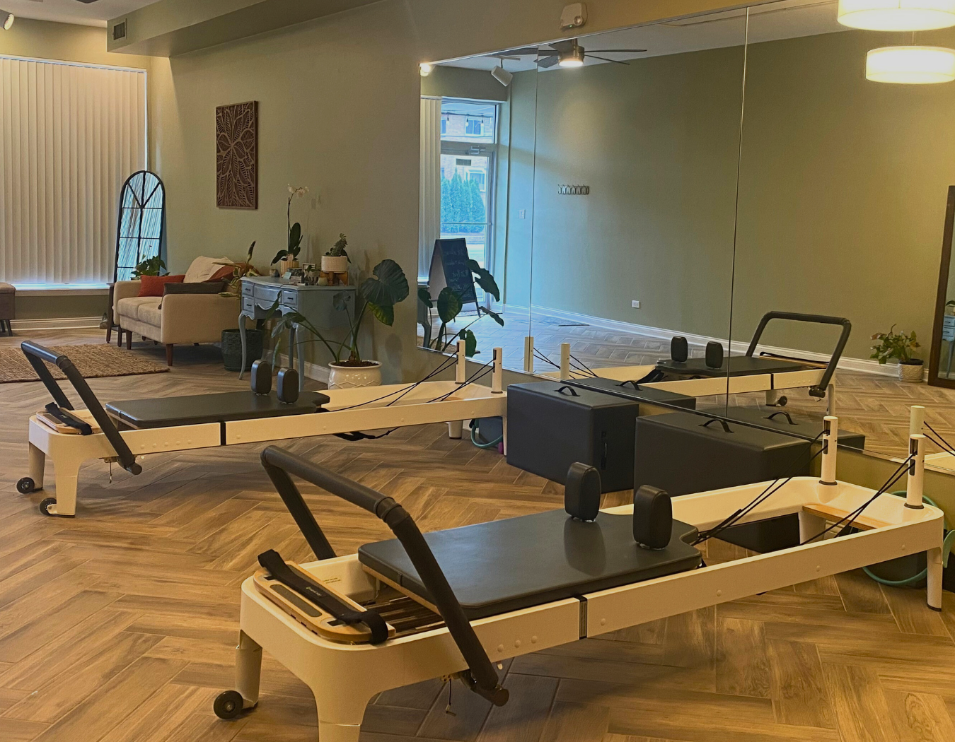 Cat's Core Pilates studio with reformer equipment and a living area with a sofa, plants, and mirror wall.