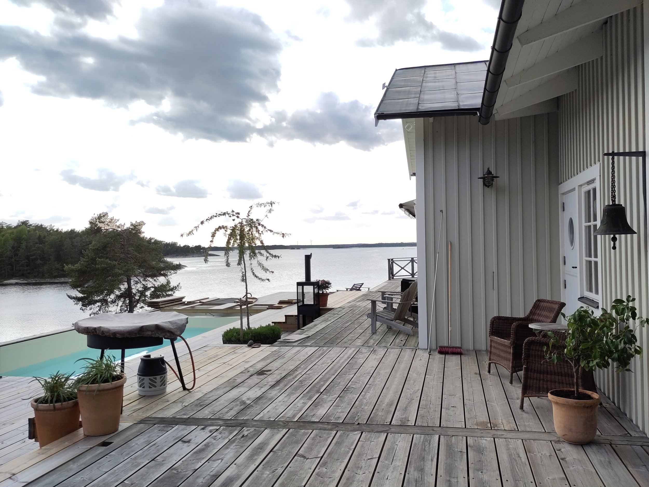 Bild av en terrass med utsikt över en sjö. Det finns två rottingstolar, ett parasoll, potted växter och en liten pool.