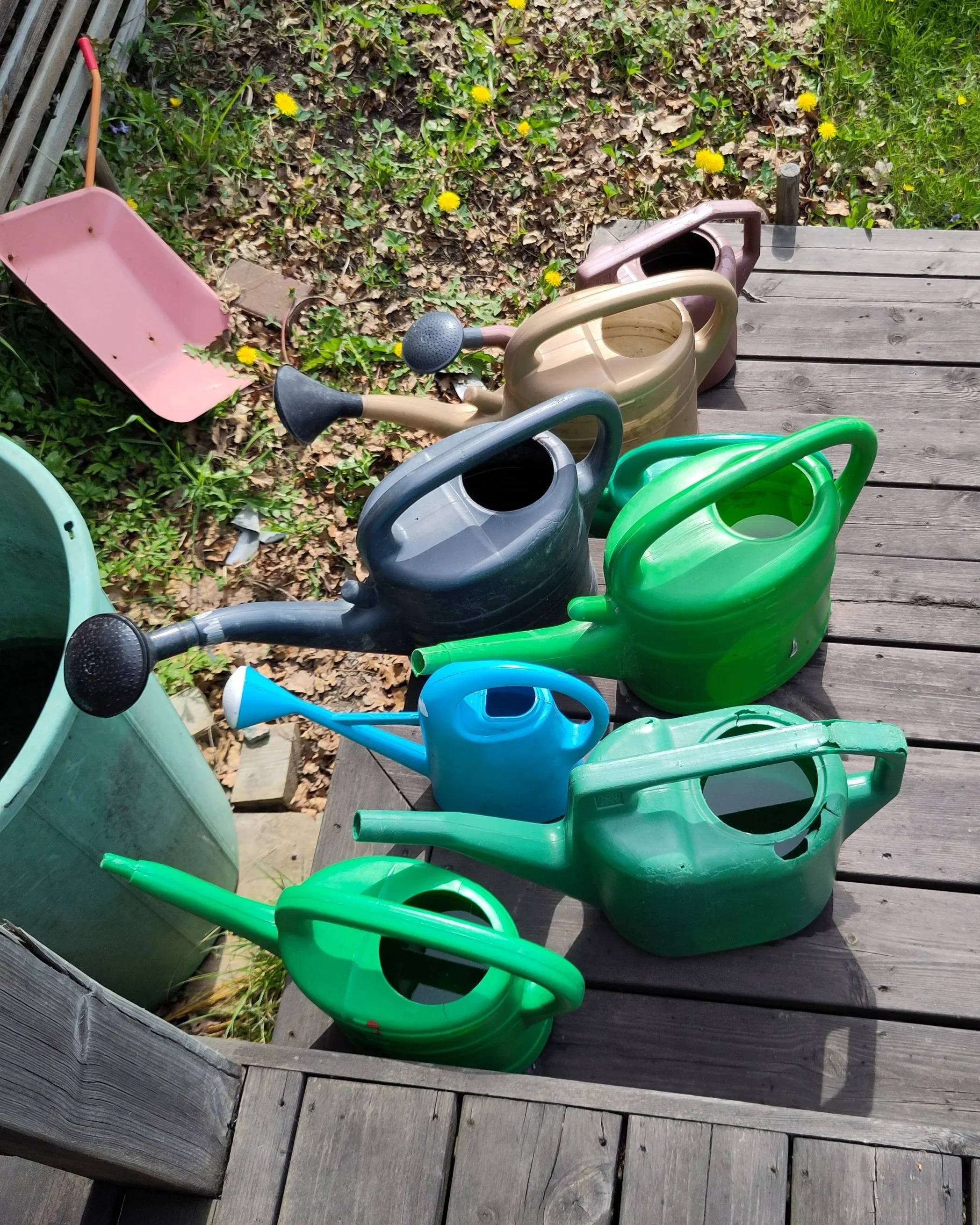 En rad av färgade plastspolkrullar och vattenkannor på en träplattform utomhus.