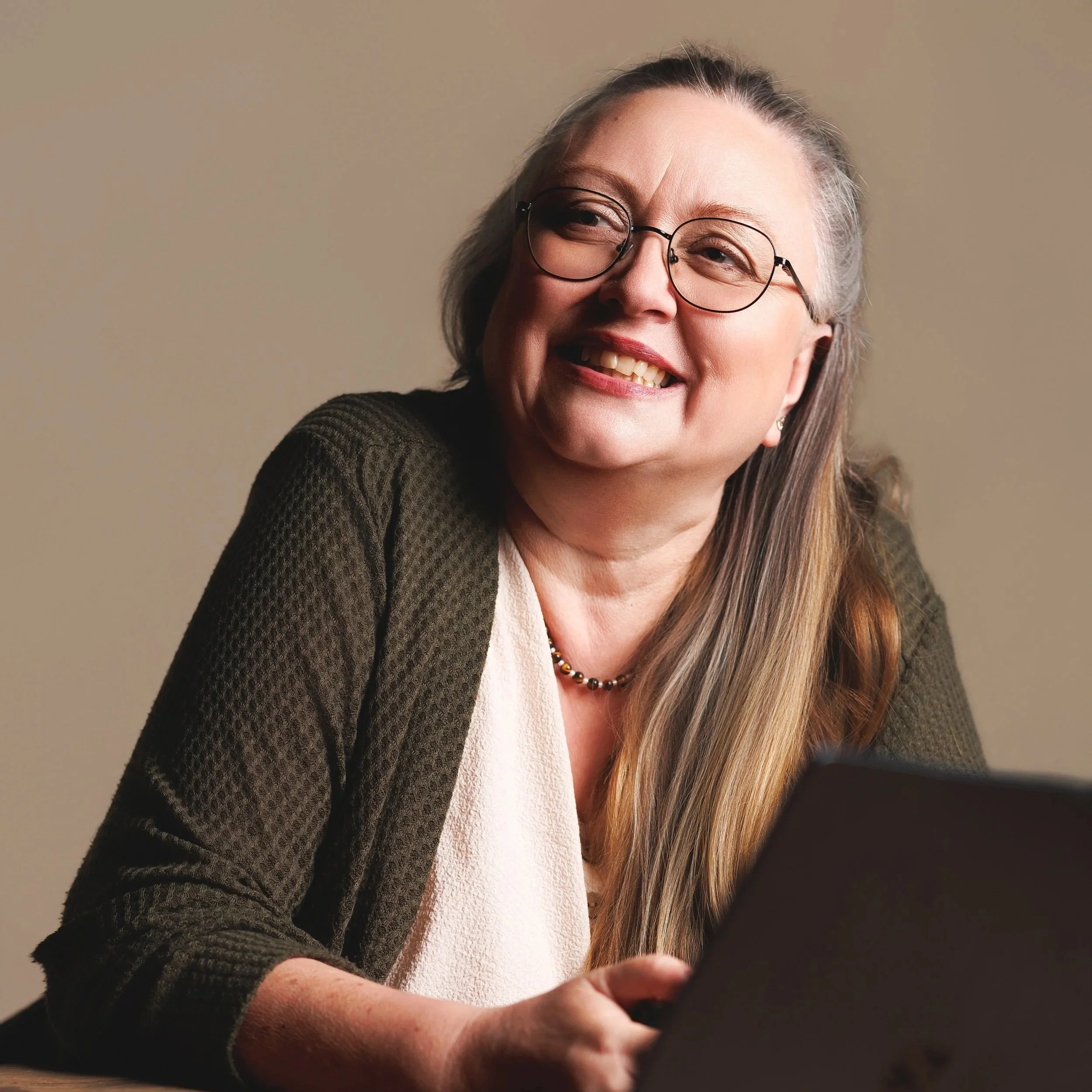 Close-up of a smiling woman with glasses using a tablet or phone.