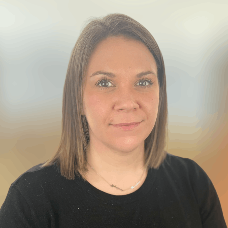 A woman with shoulder-length brown hair and brown eyes, smiling slightly, wearing a black top and a delicate necklace, against a blurred beige and light gray background.