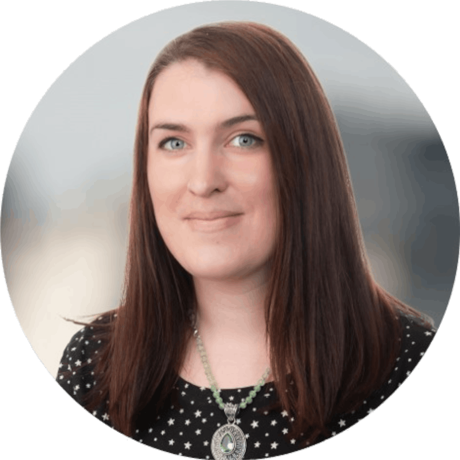 Portrait of a woman with long brown hair, wearing a black top with white polka dots and a beaded necklace with a large circular pendant.