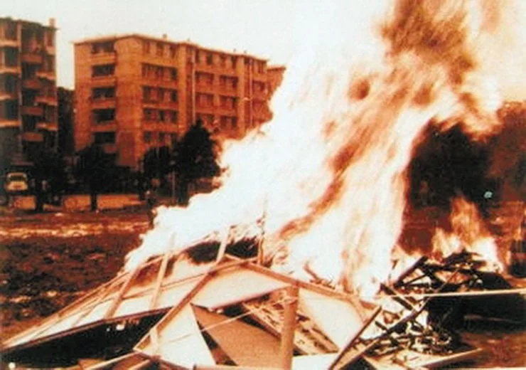 A building on fire with large flames and smoke, wreckage and debris scattered on the ground.