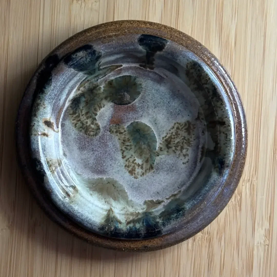 En keramikassiett med intrikat mönster, rå lera och hög kant på ett träbord.