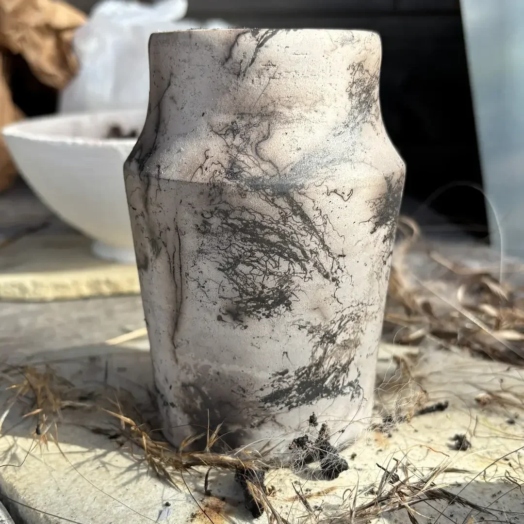 En beige och svart keramikkruka på en träskiva, omgiven av andra keramikkärl.