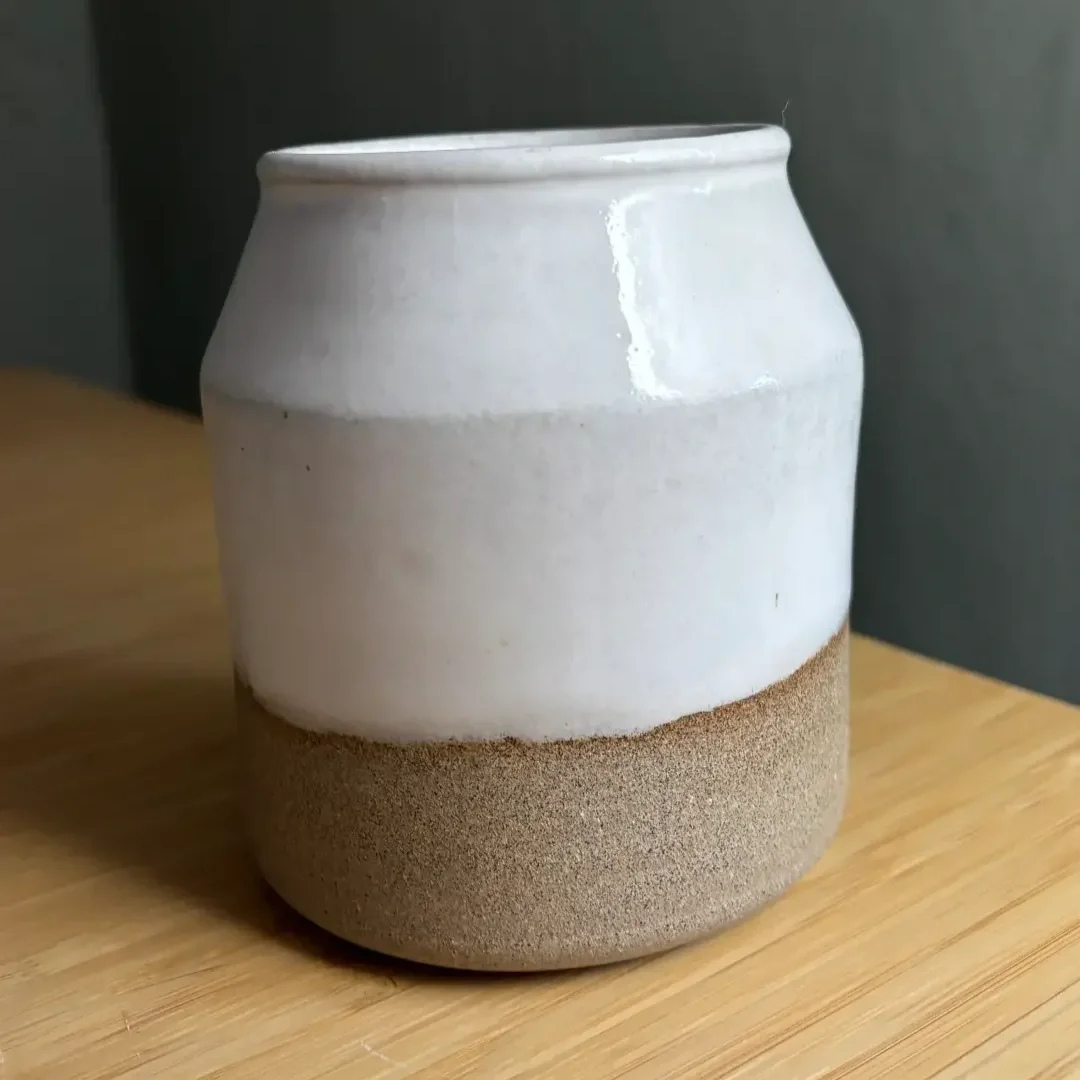 En vit och sandfärgad keramikvas på ett träbord.