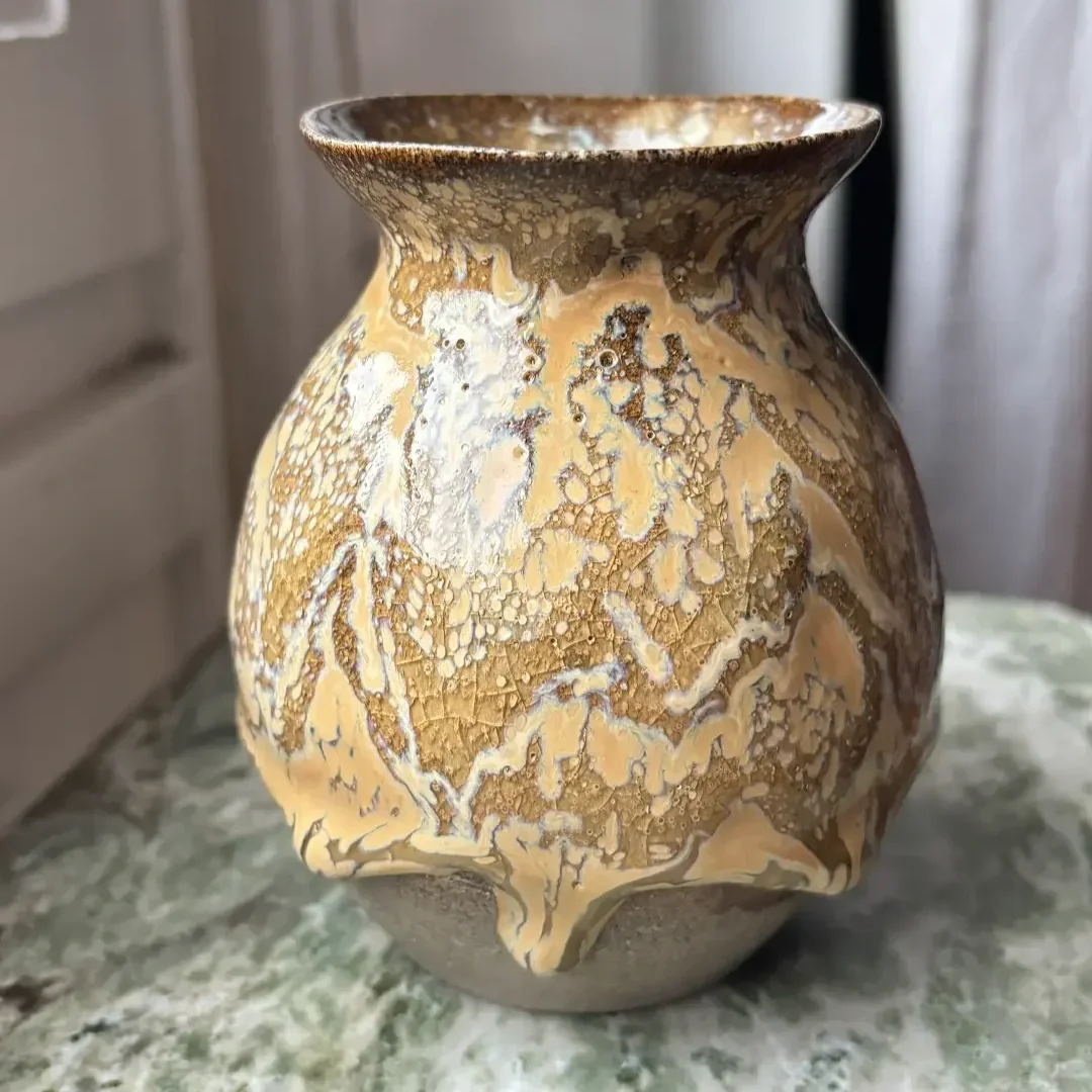 Rund vas med utsvängd hals med krackelerad glasyr placerad på ett ljust trädskrivbord.