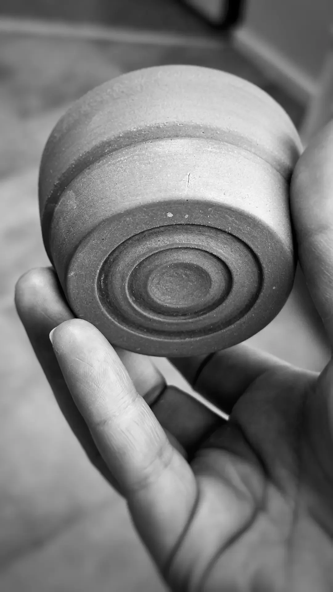 Svartvit bild på ett keramiskt verks undersida. Händer som håller i asken.