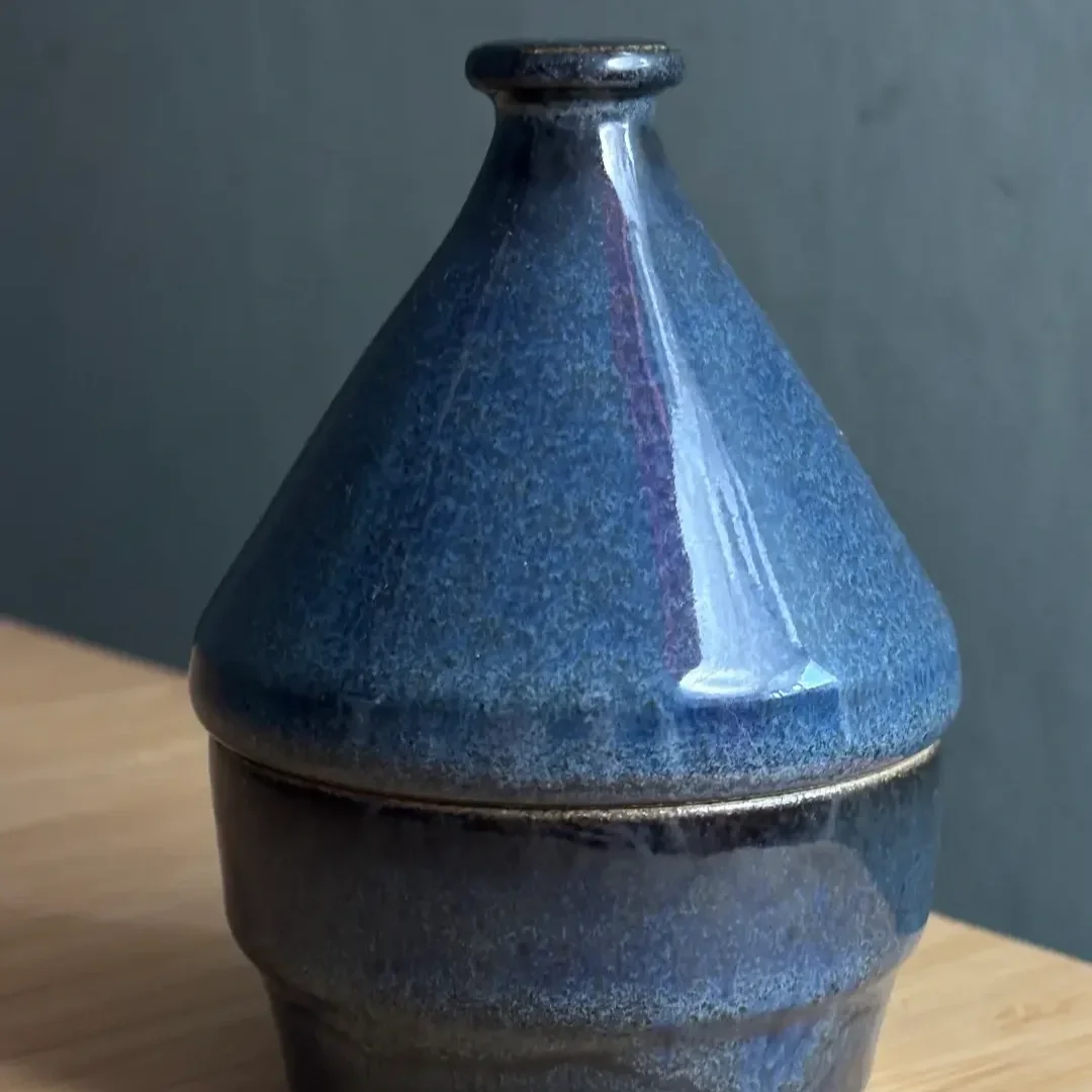 En mörkblå keramikask med lock på ett träbord.