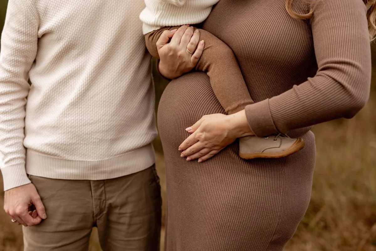 Ein schwangeren Frau, die einen kleinen Jungen auf ihrem Arm hält, während ein Mann neben ihnen steht.