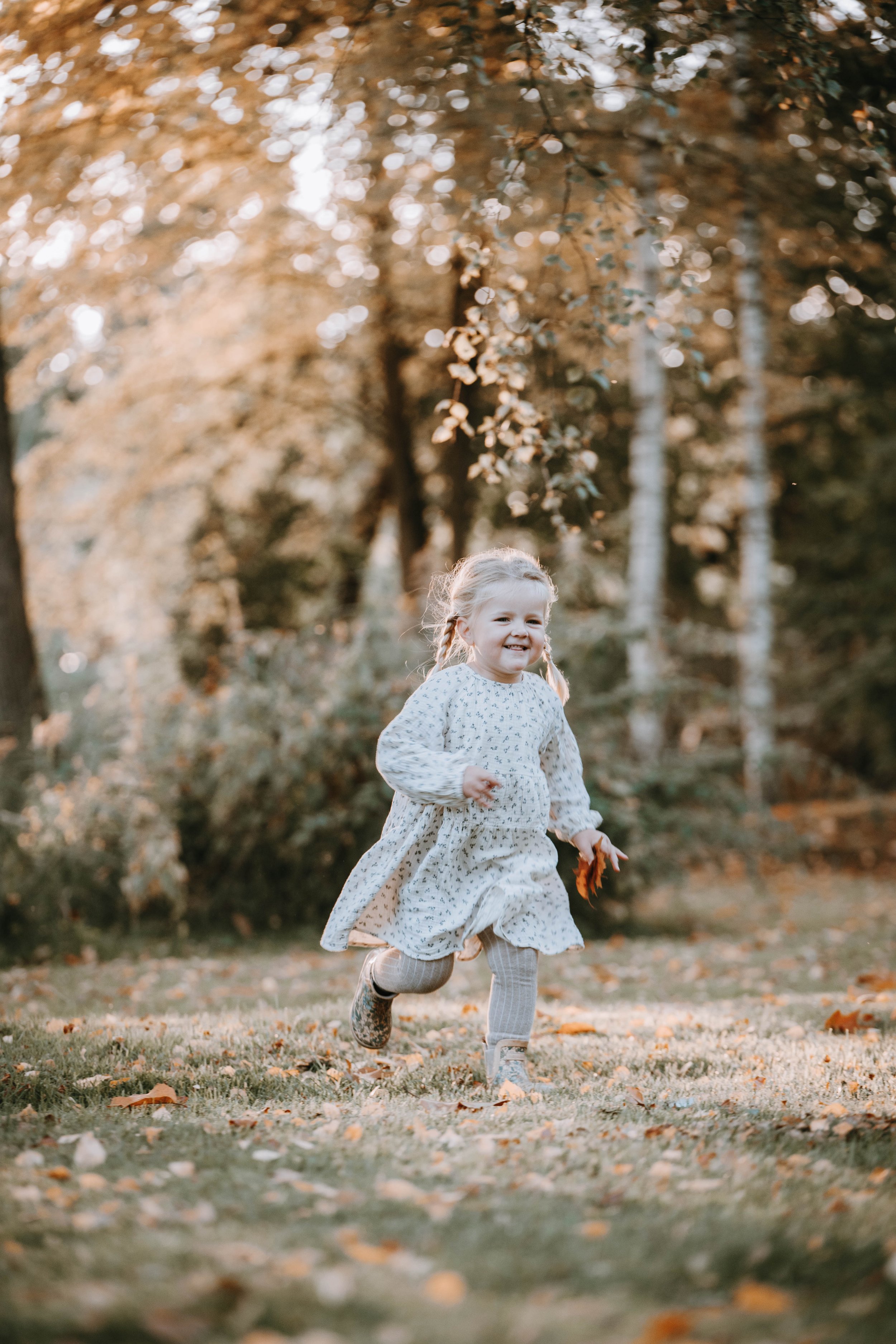 Ein lachendes kleines Mädchen läuft im Park mit herbstlichem Laub."