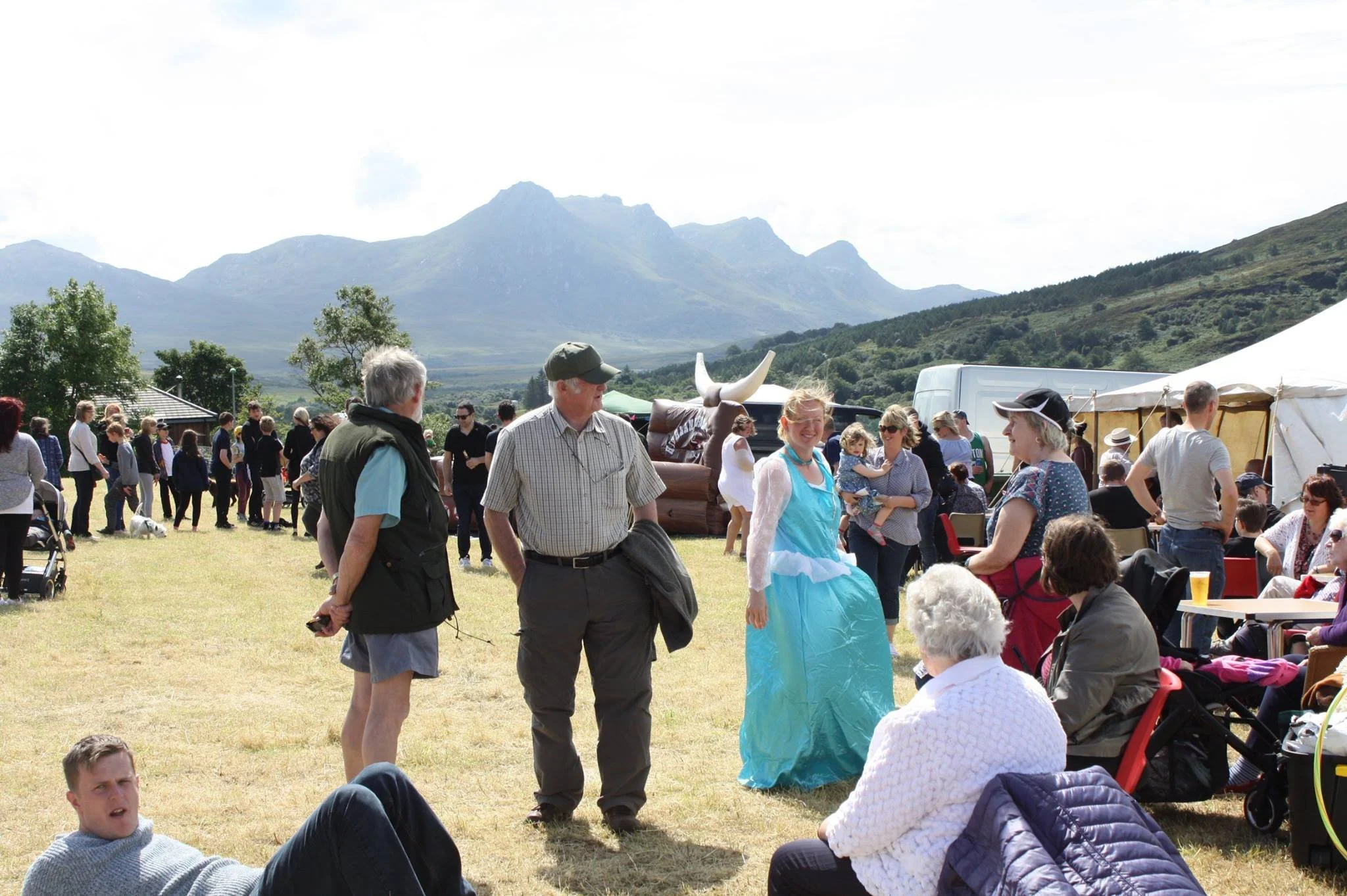 People gathered outdoors at a community event in Tongue with a backdrop of Ben Loyal, a Marquee, and a blue sky.