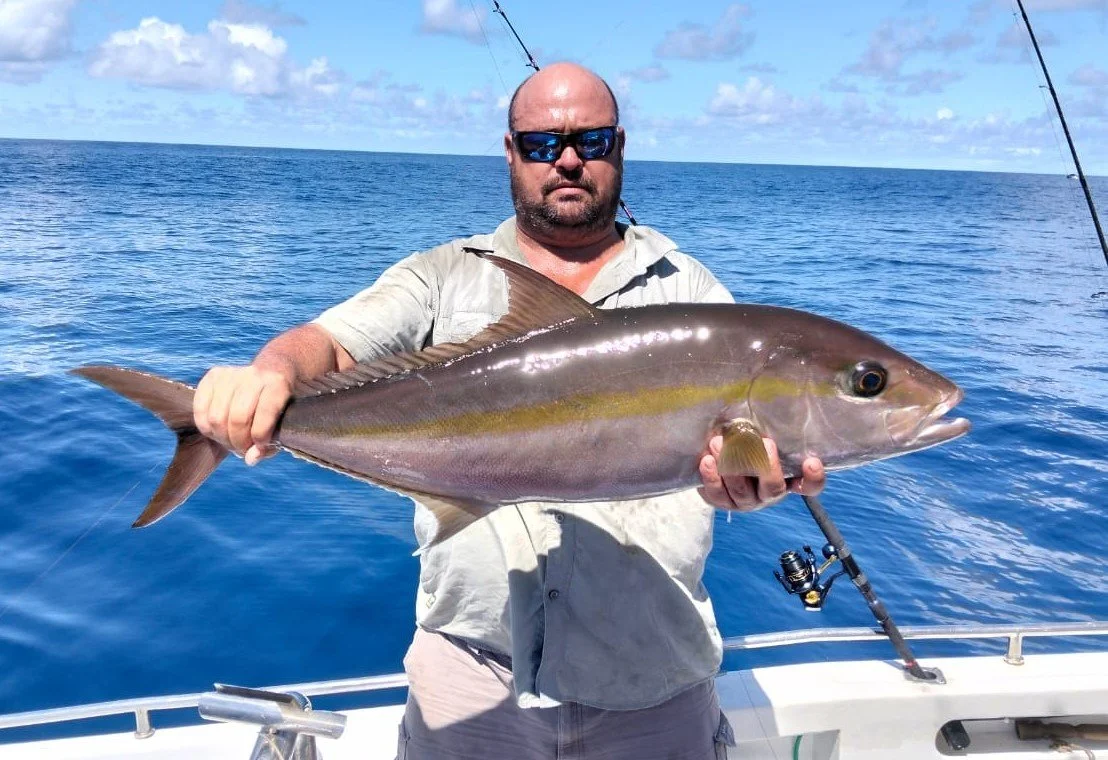 Man on a boat holding a large fish, with the ocean and blue sky in the background.