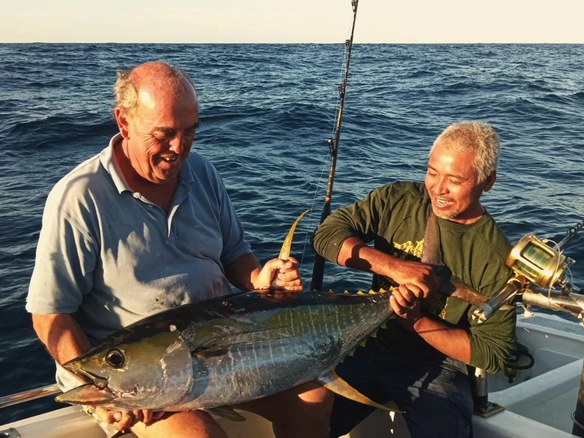 Two men on a boat holding a large fish between them, smiling, with the ocean in the background.