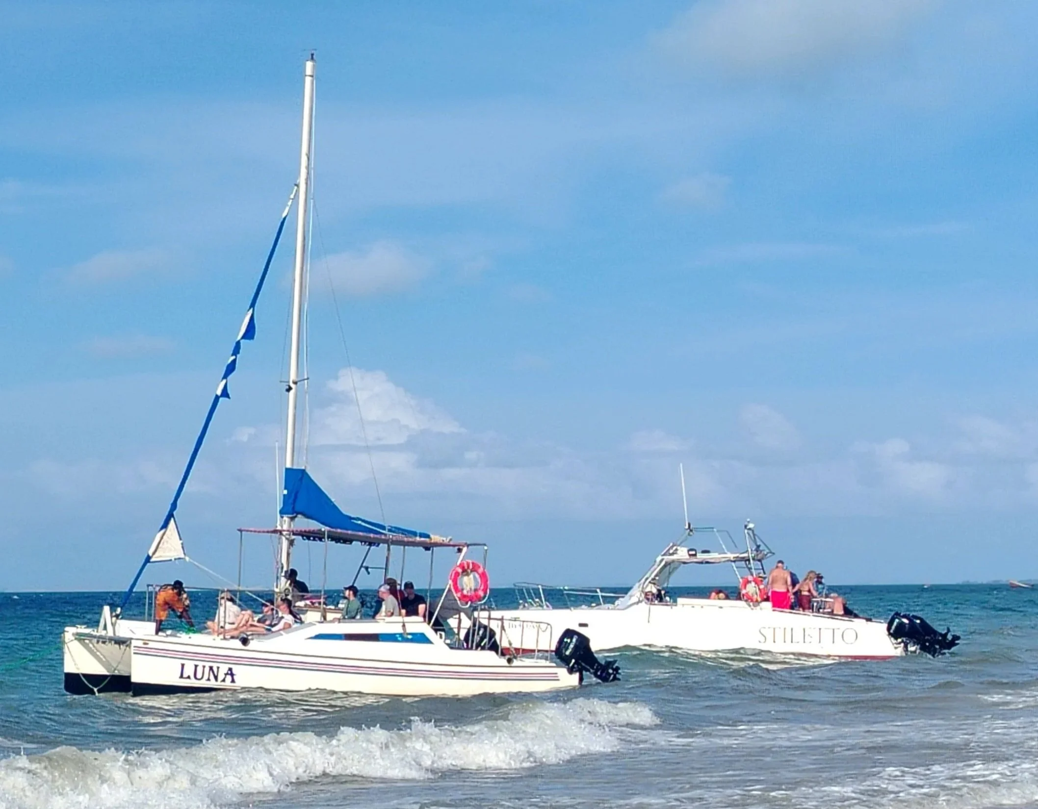 People relaxing and enjoying a boat cruise on a white sailboat named Luna on calm water, with other boats and a clear blue sky in the background.