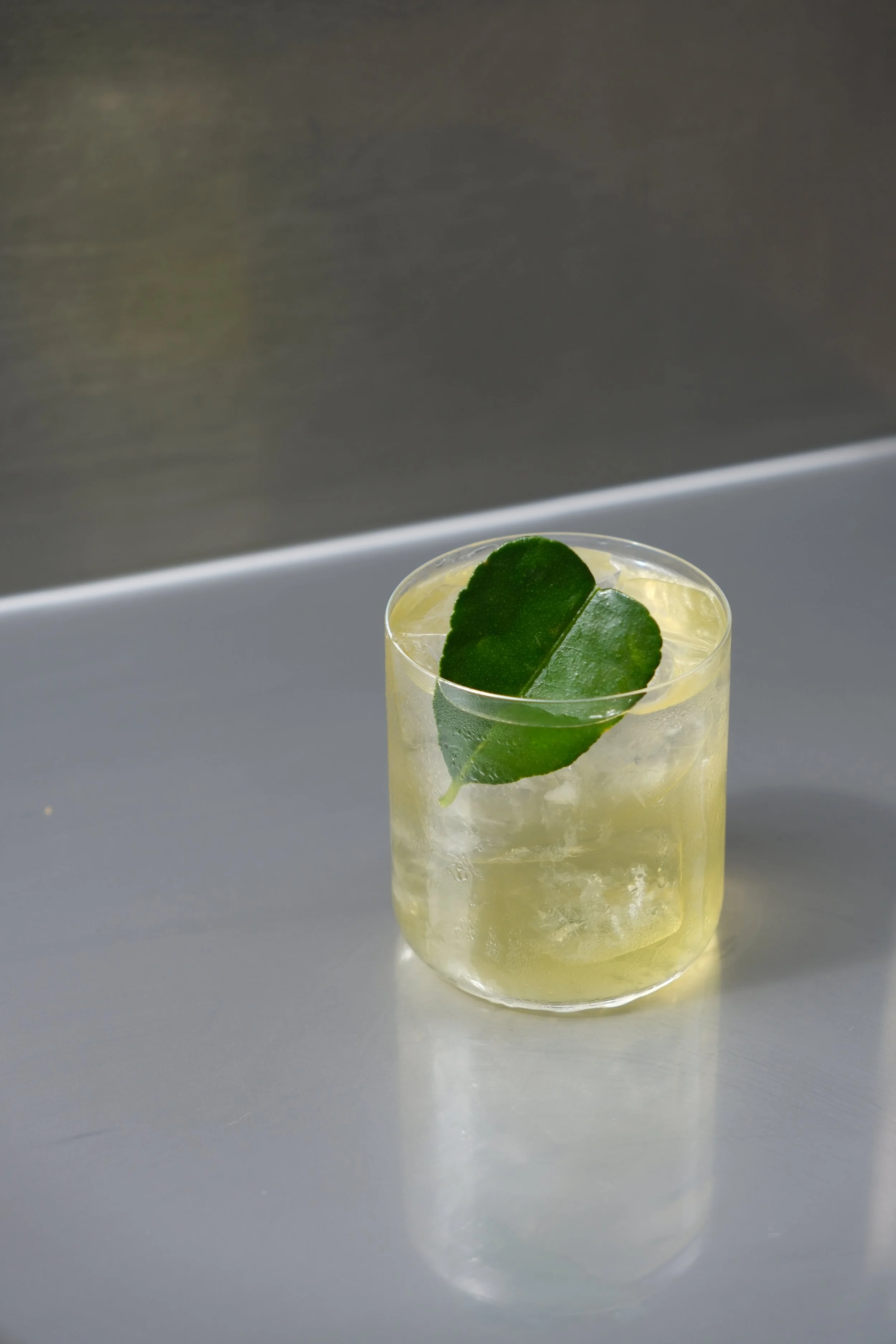 Un verre contenant une boisson claire, des glaçons et une feuille de citron vert