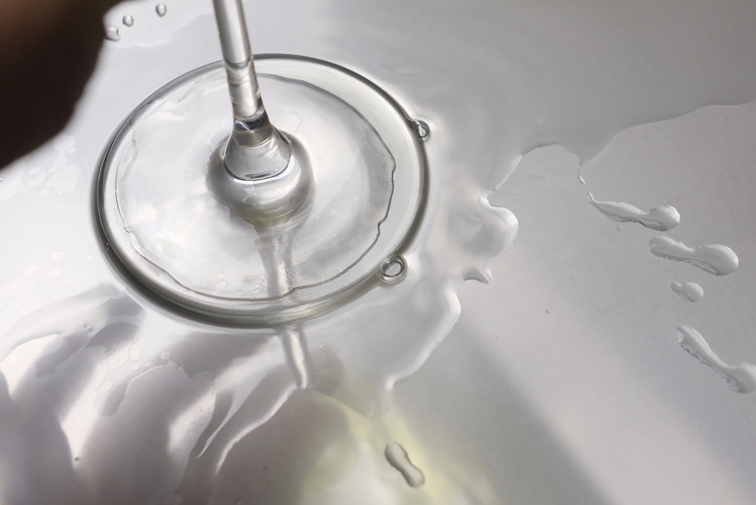 Goutte de liquide en chute dans un récipient en verre, avec des éclaboussures blanches sur une surface métallique ou en plastique