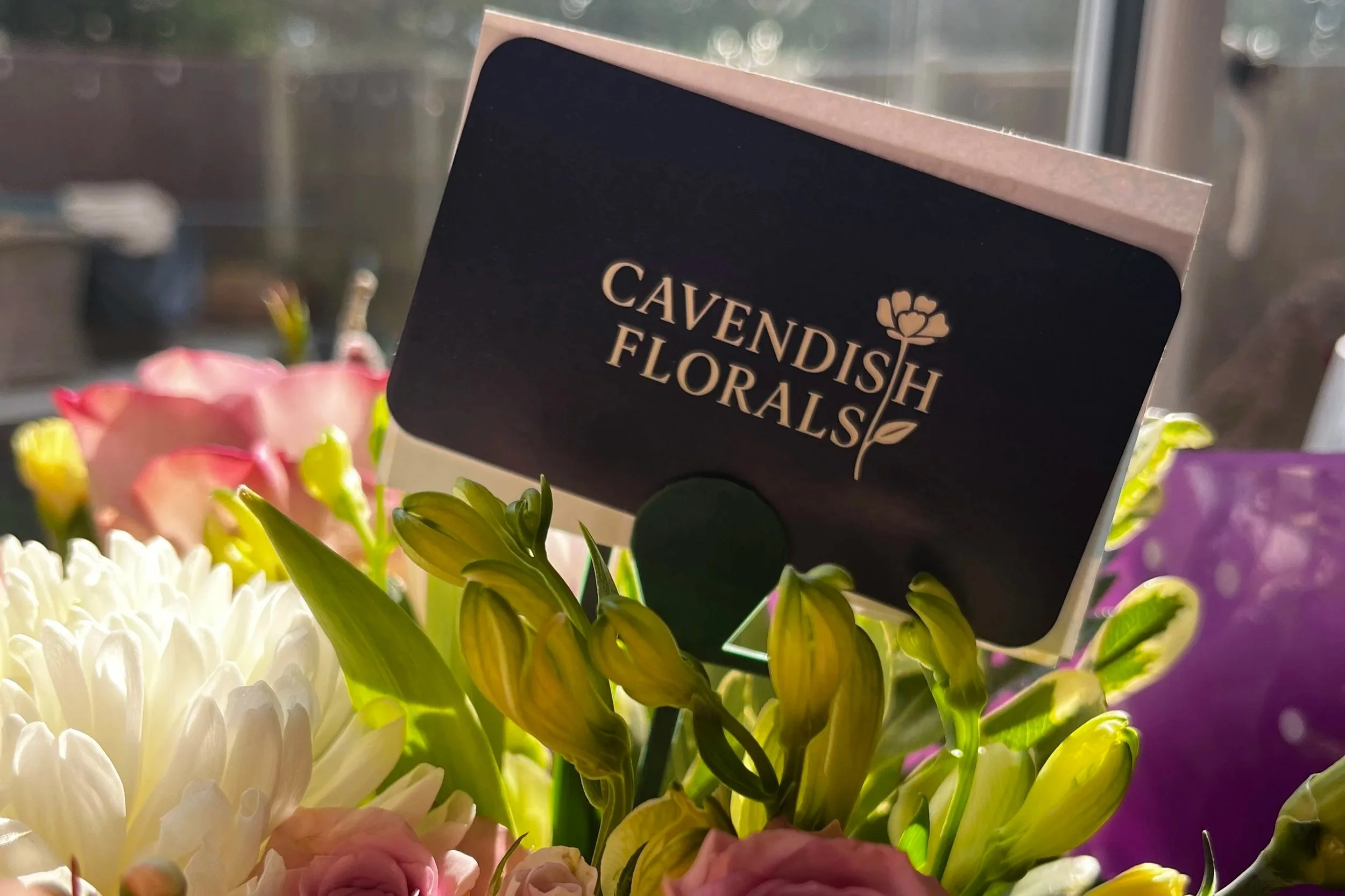 A flower arrangement from Cavendish Florals includes pink roses, white chrysanthemums, and yellow lilies with a black and pale pink sign.