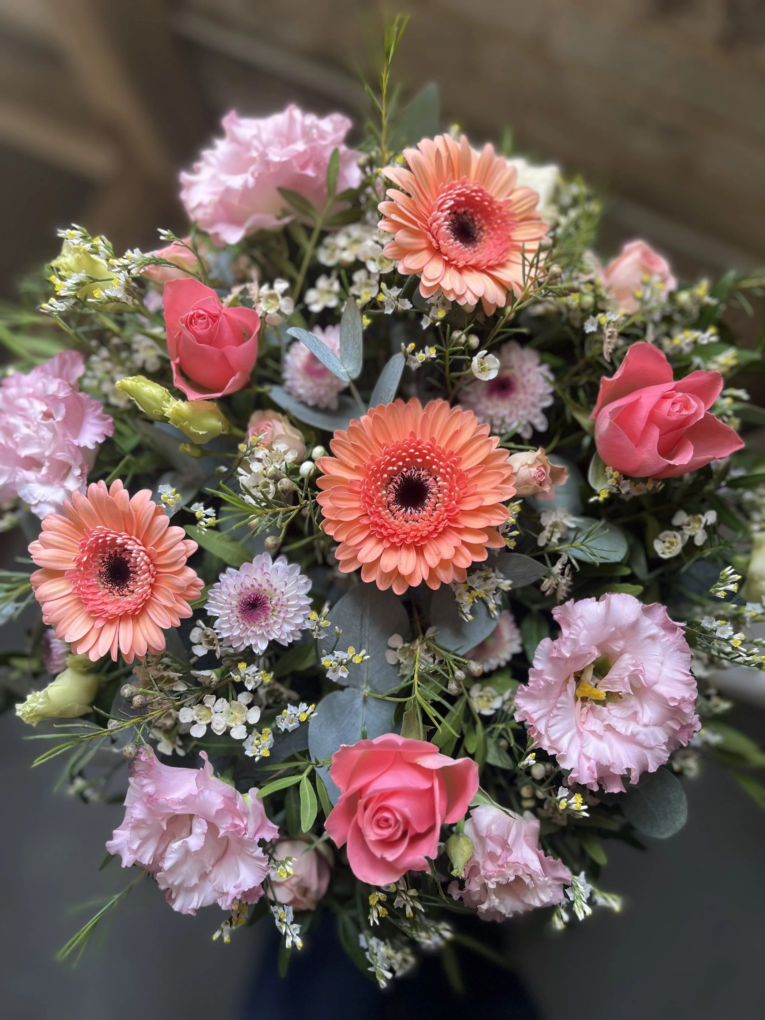 A colorful bouquet of pink, peach, and white flowers including gerbera daisies, roses, lisianthus, and baby's breath, with green foliage.