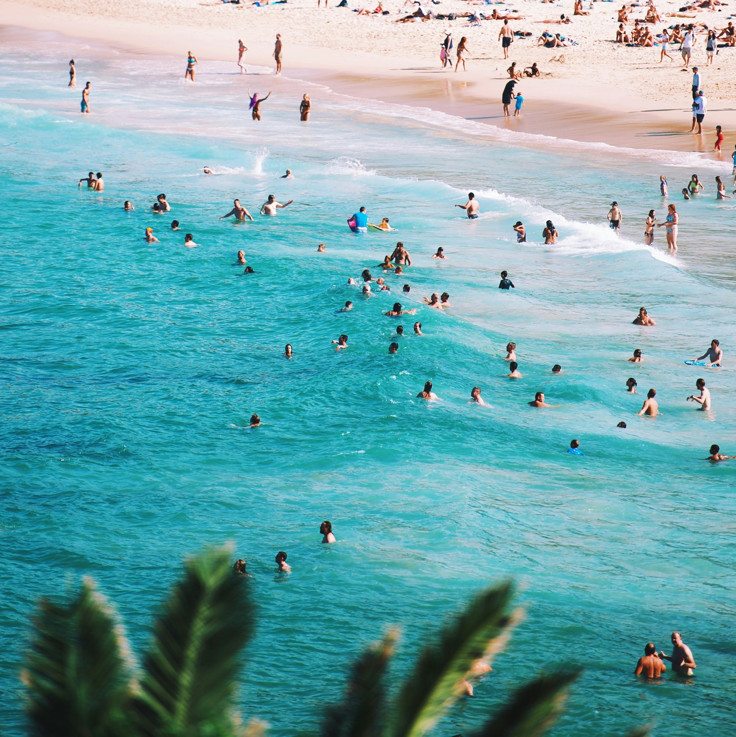 People swimming and relaxing on a sandy beach with clear blue water.