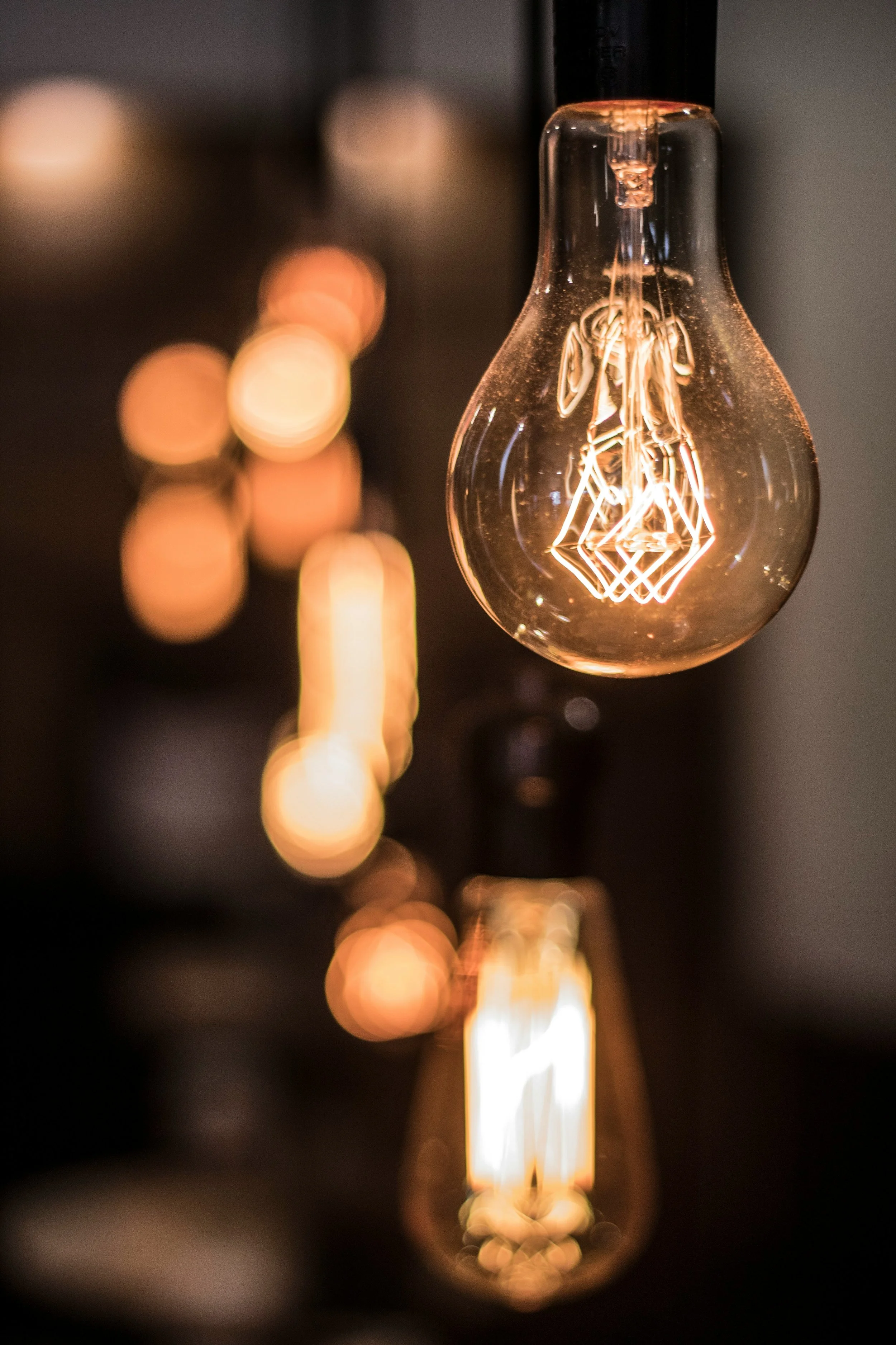 Close-up of vintage-style Edison lightbulbs with filament visible, hanging in a dark room, creating a warm glow.
