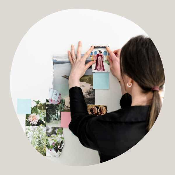 Back of woman arranging some pictures in a collage on the wall. Woman is wearing black and has her brown hair tied in a ponytail with a brown band.
