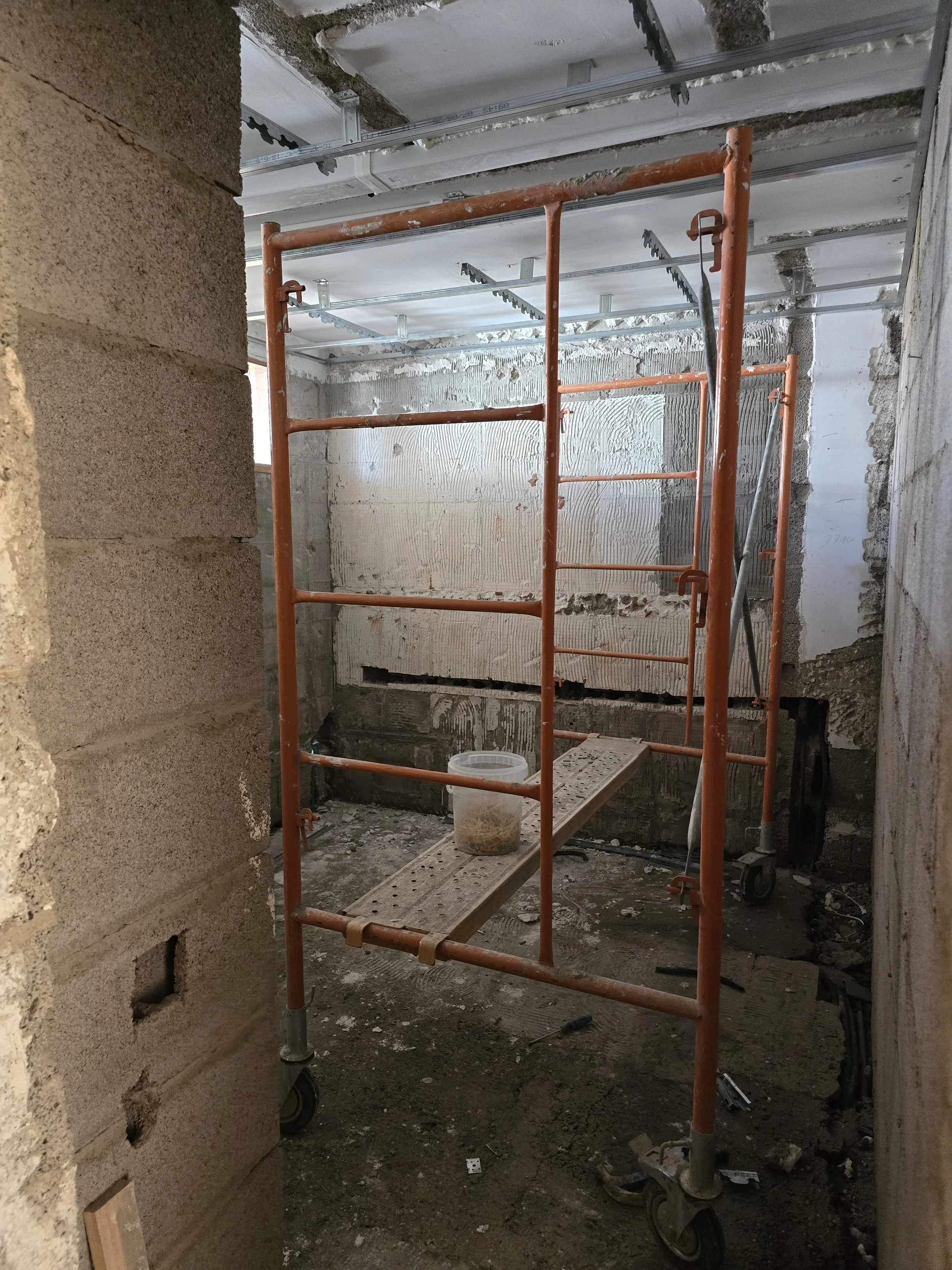 Construction site with orange scaffolding, unfinished walls, and construction materials on the floor.