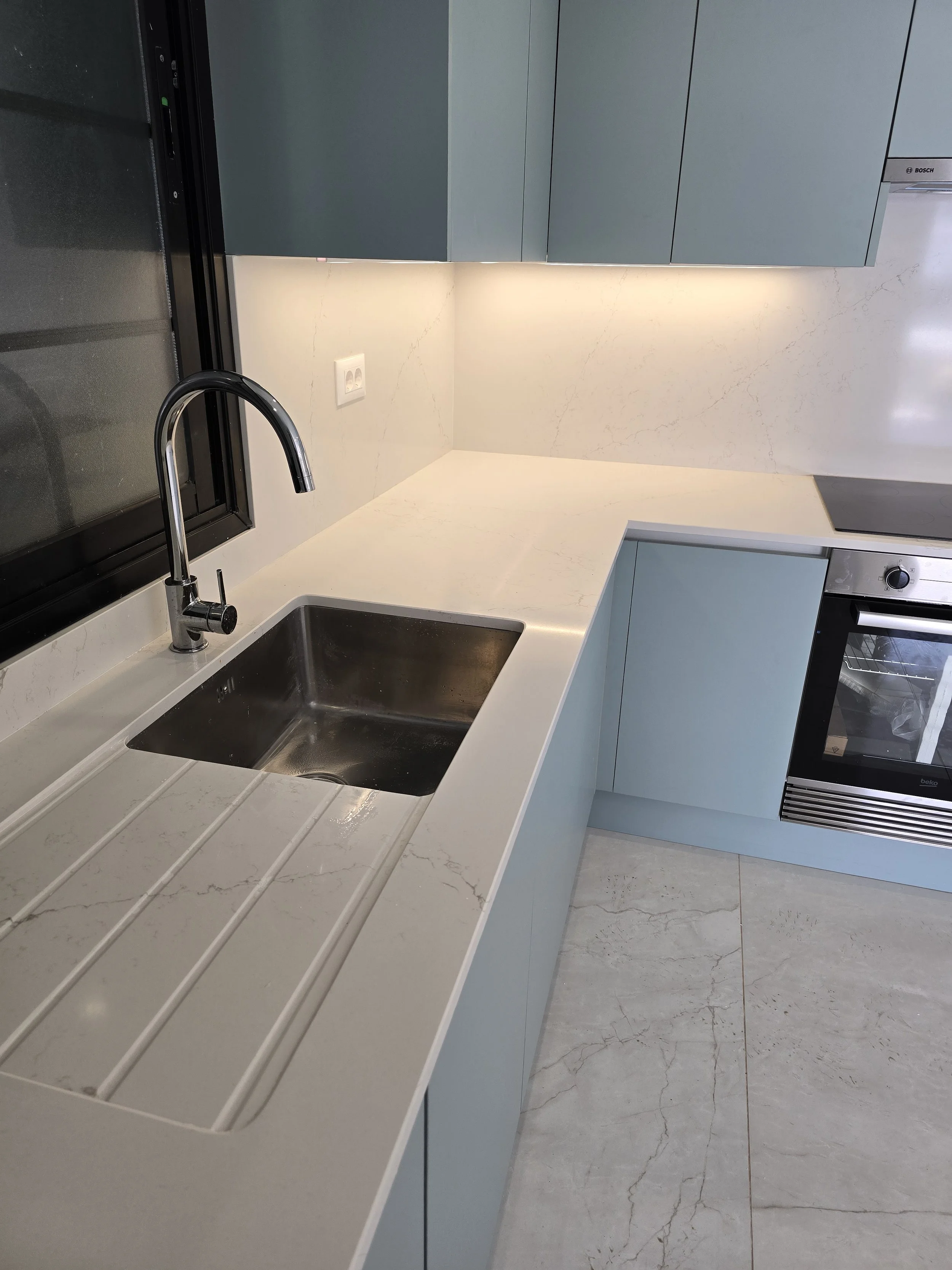 Modern kitchen with a white marble countertop, stainless steel sink, black faucet, blue cabinets, and built-in oven.