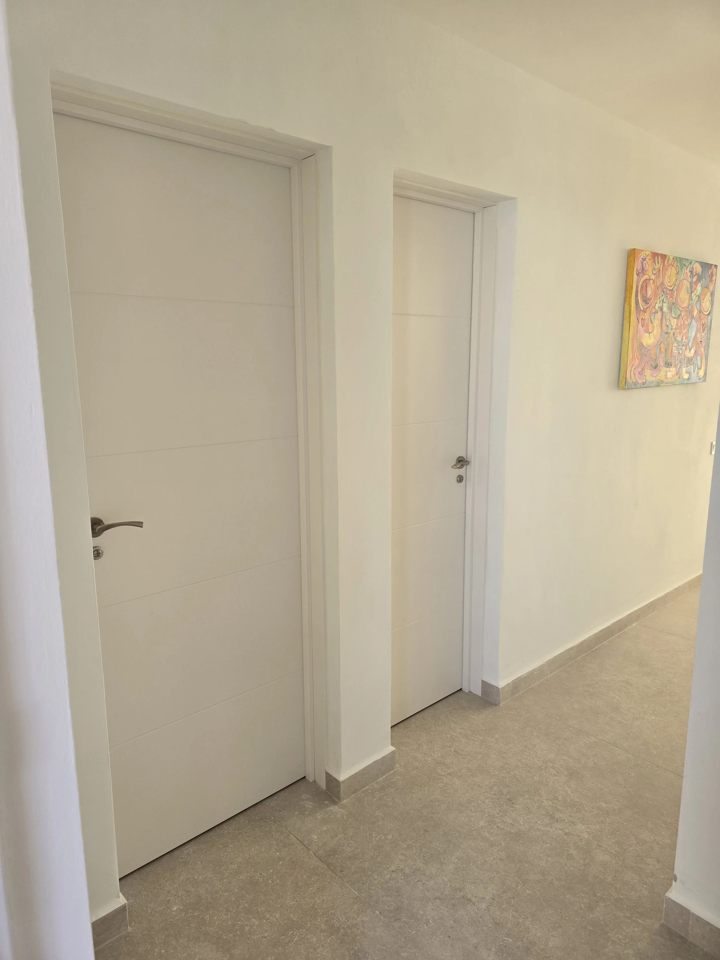 A hallway with two closed white doors and a colorful abstract painting on the wall.