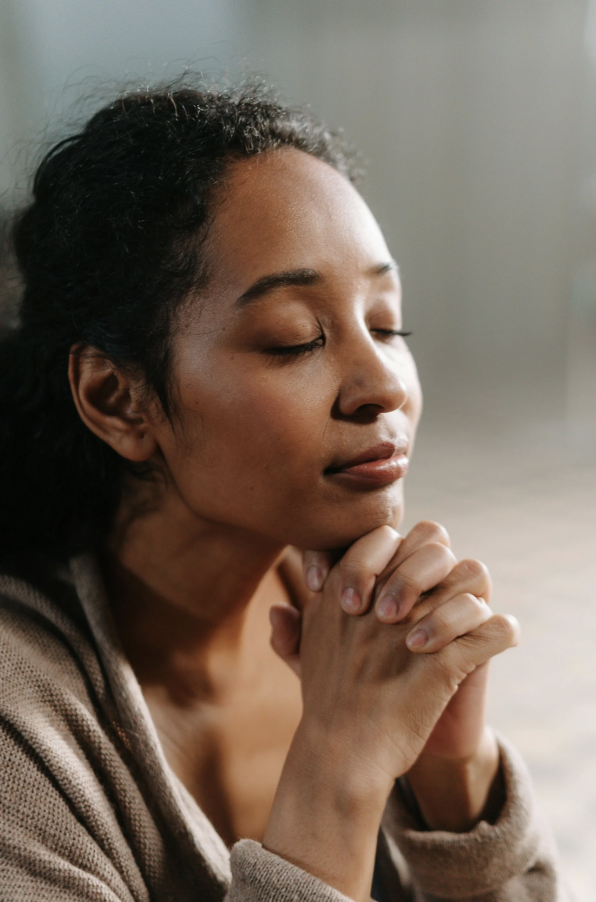 A woman with closed eyes holding her hands together under her chin, appearing to be in prayer or meditation. She is the client of Megan Bradley therapy, the best therapist in Amsterdam.