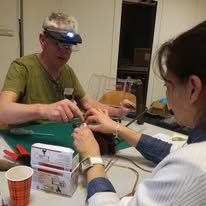 Twee mensen die hand-naar-hand contact maken tijdens een activiteit, met sieraden en zaklampen op een tafel met gereedschap en een kleine doos.