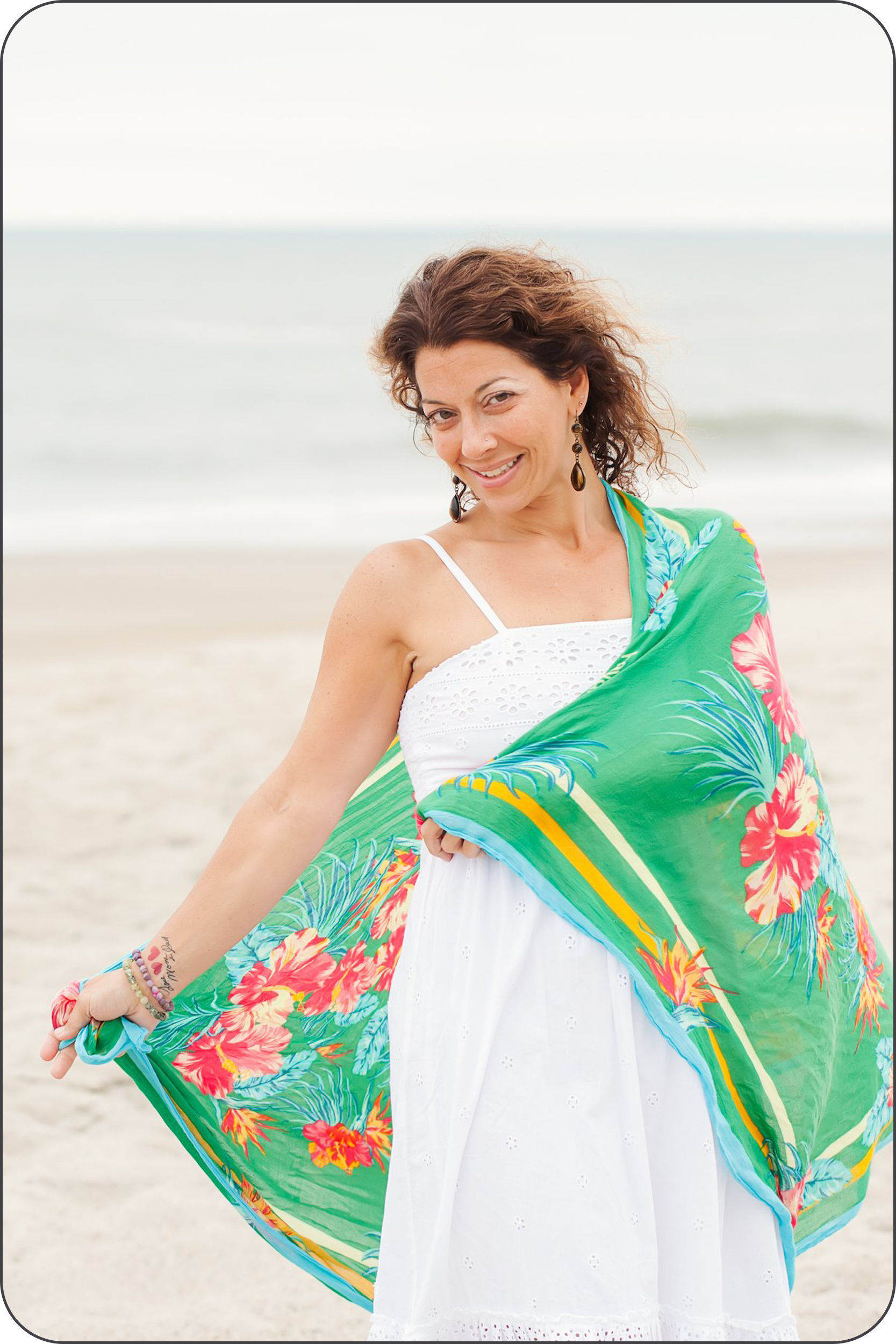 Deanna Scaldaferri, professional life coach and founder of Healing Hands by Deanna LLC, wearing a green scarf at the beach. Her relaxed and happy expression represents the heart-centered healing and growth she facilitates for her clients.