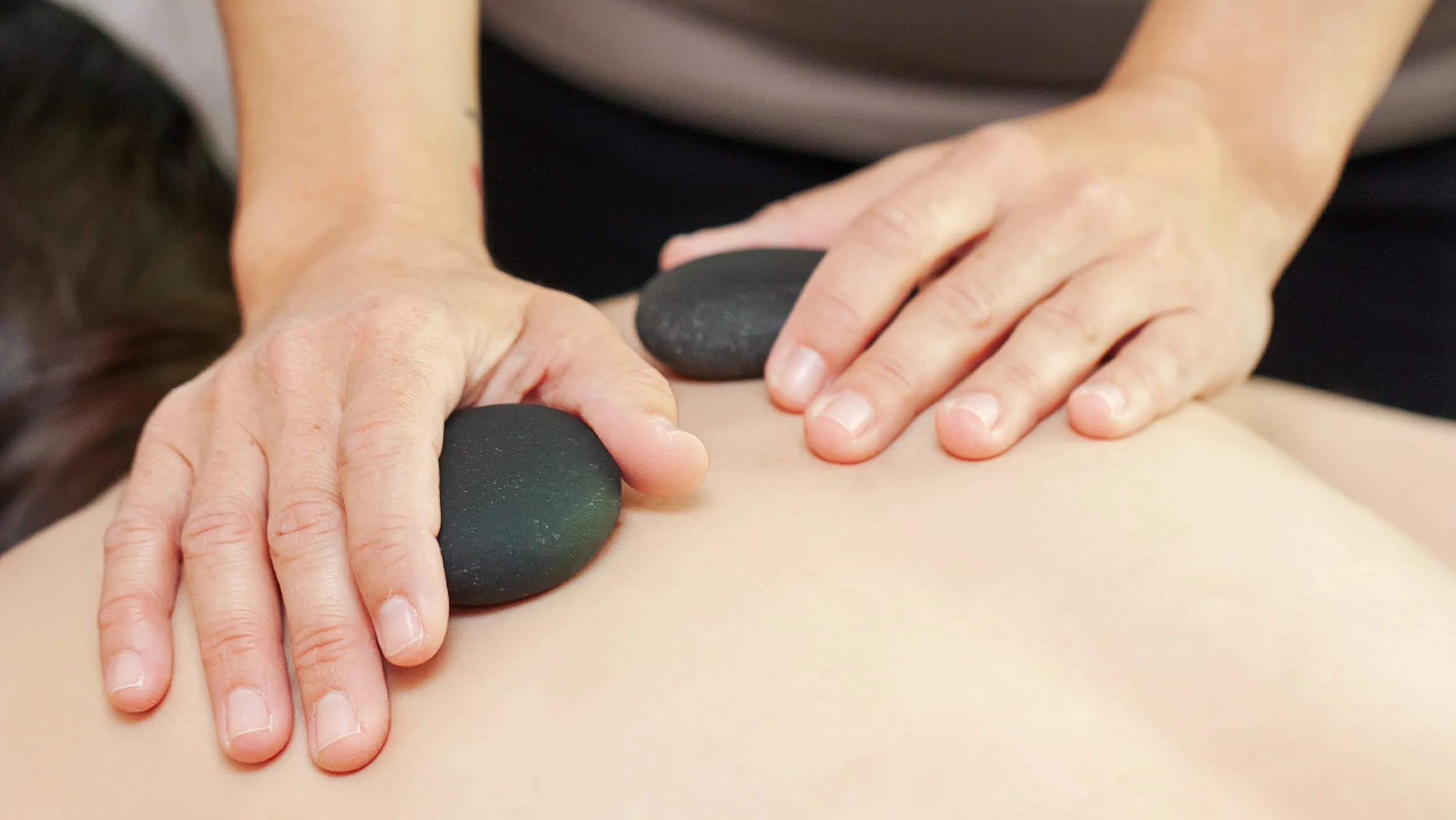 Close-up of Deanna's hand placing smooth, heated basalt stones on a client's back during a professional hot stone massage session.