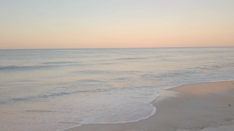 A serene GIF of gentle ocean waves washing onto the shore, representing the calm, stress-relieving atmosphere of a massage and Reiki session with Deanna Scaldaferri in Charlotte.