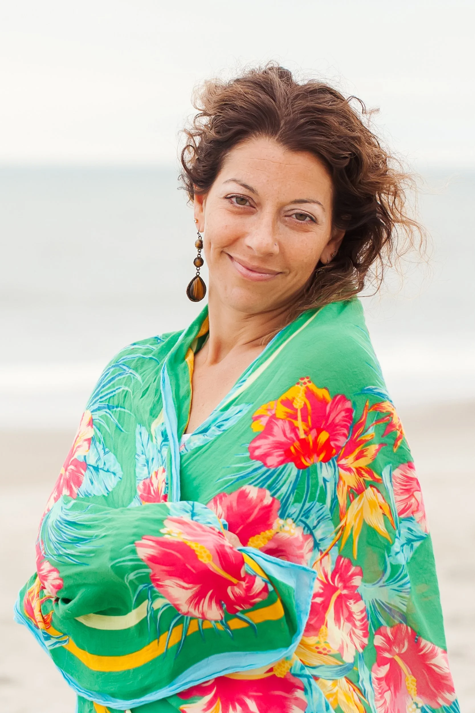 Deanna Scaldaferri, a Charlotte Reiki Master, wrapped in a green scarf on the beach, symbolizing the nurturing environment and heart-centered healing provided through her life coaching and Reiki sessions.