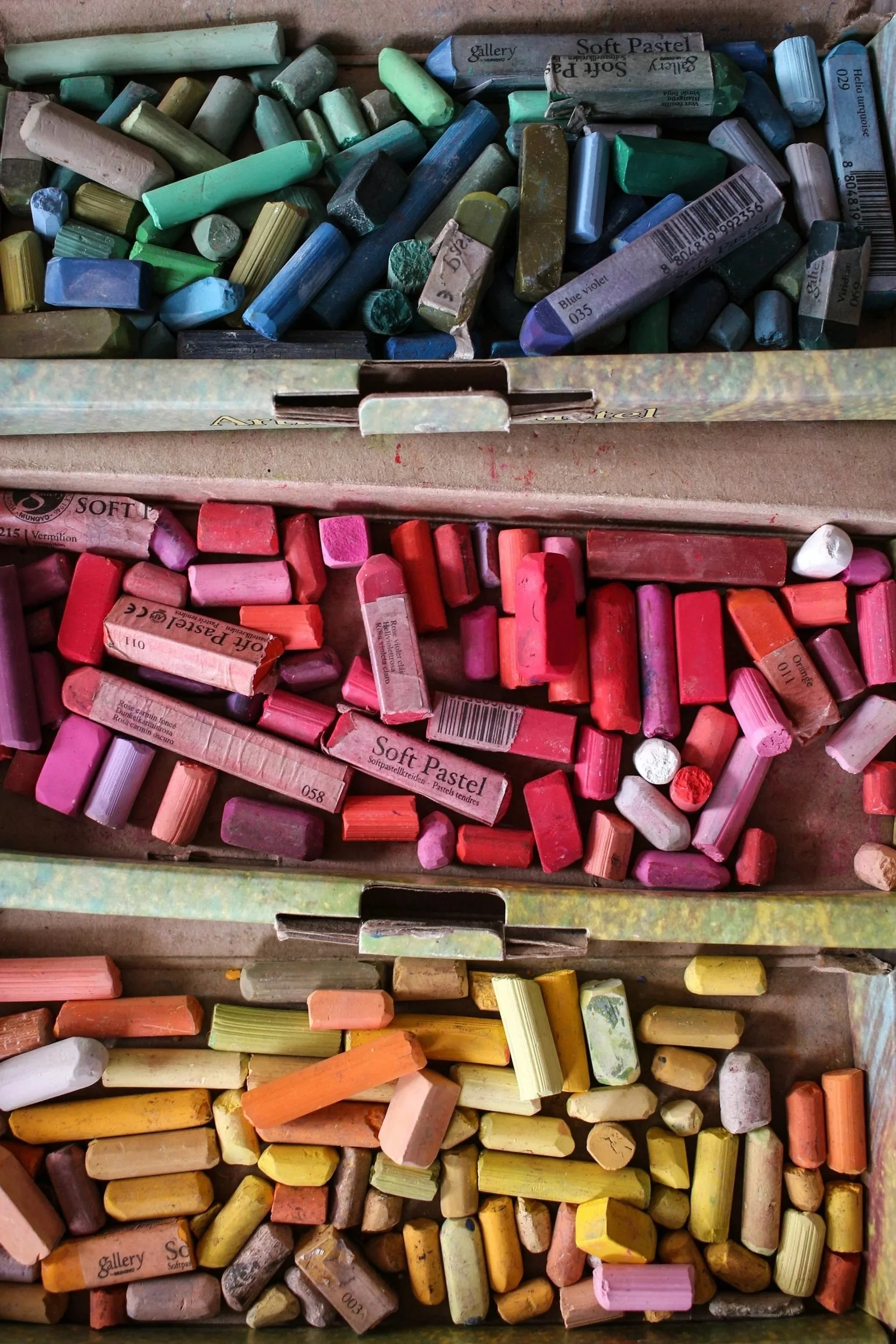 Boxes of used soft pastels in various colors, including green, pink, yellow, and orange.