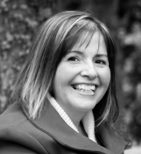 Close-up black and white portrait of a smiling woman with shoulder-length hair, outdoors background.