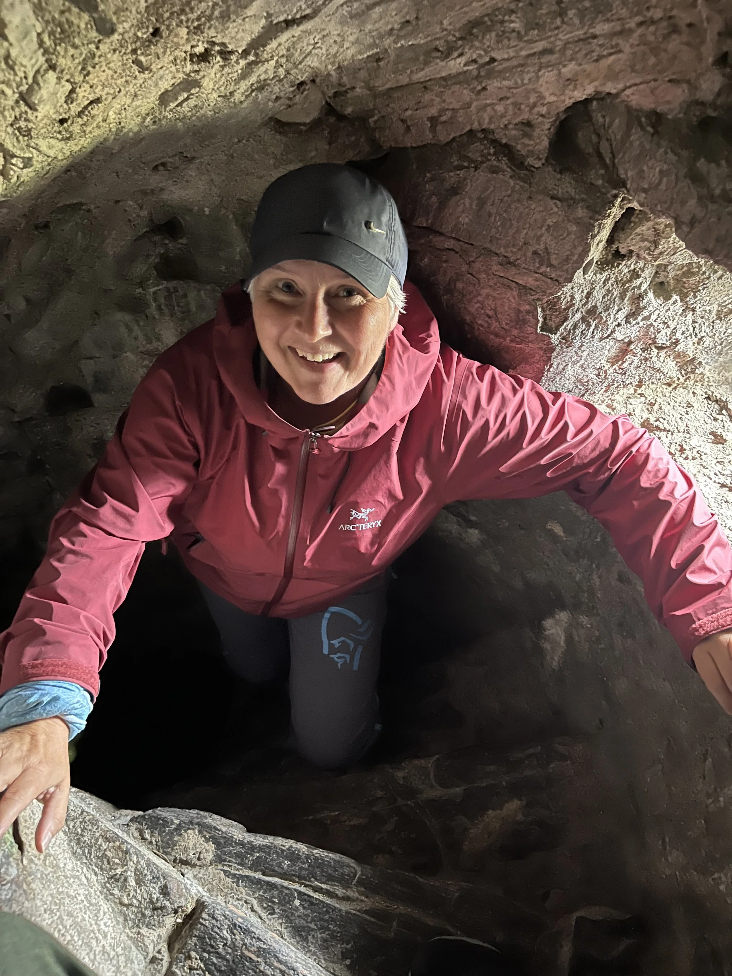 Person i rosa jakke og svart caps kryper gjennom en steinrenne.