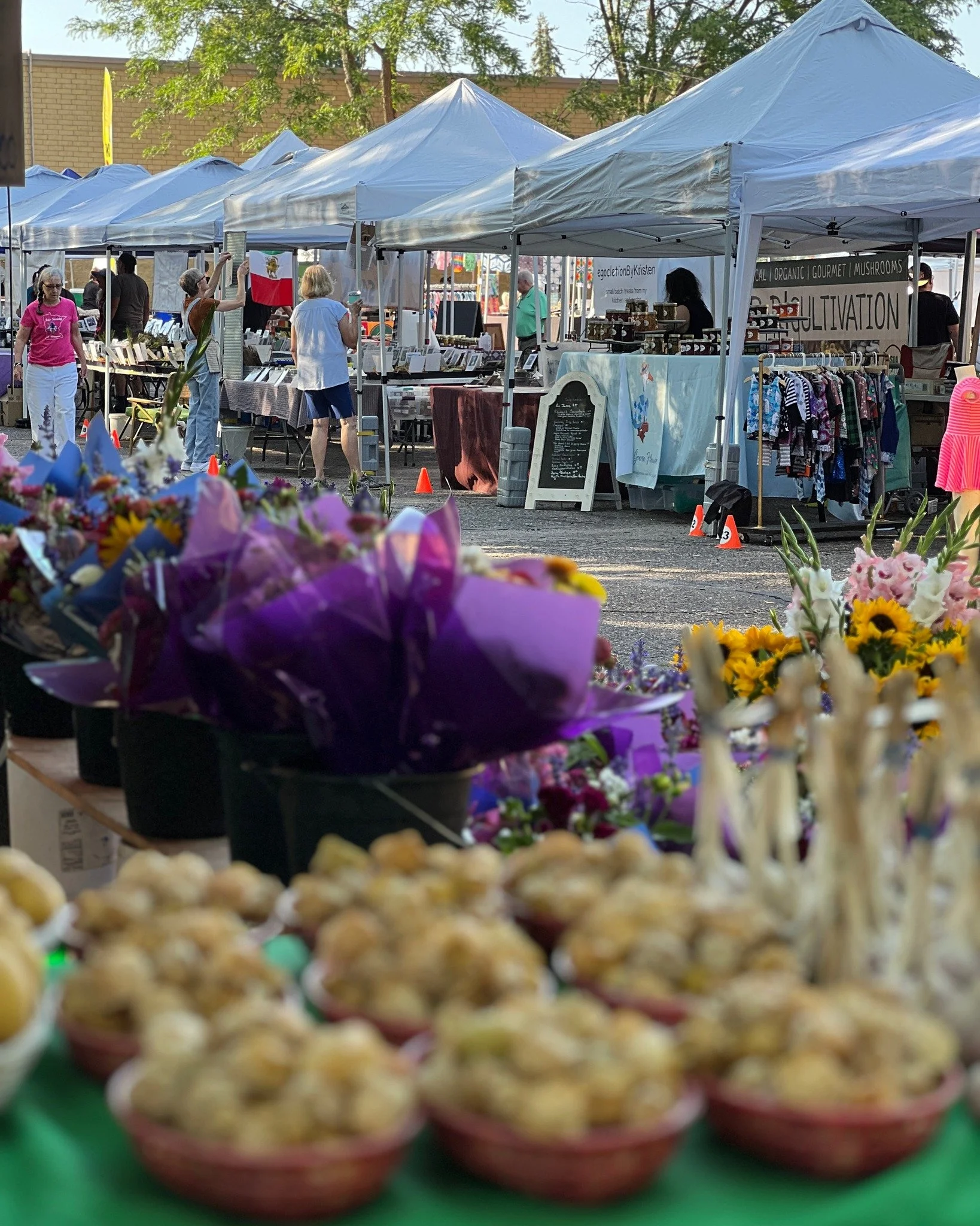 Close-up of colorful bowls filled with popcorn on a green table at an outdoor market, with blurred tents and shoppers in the background.