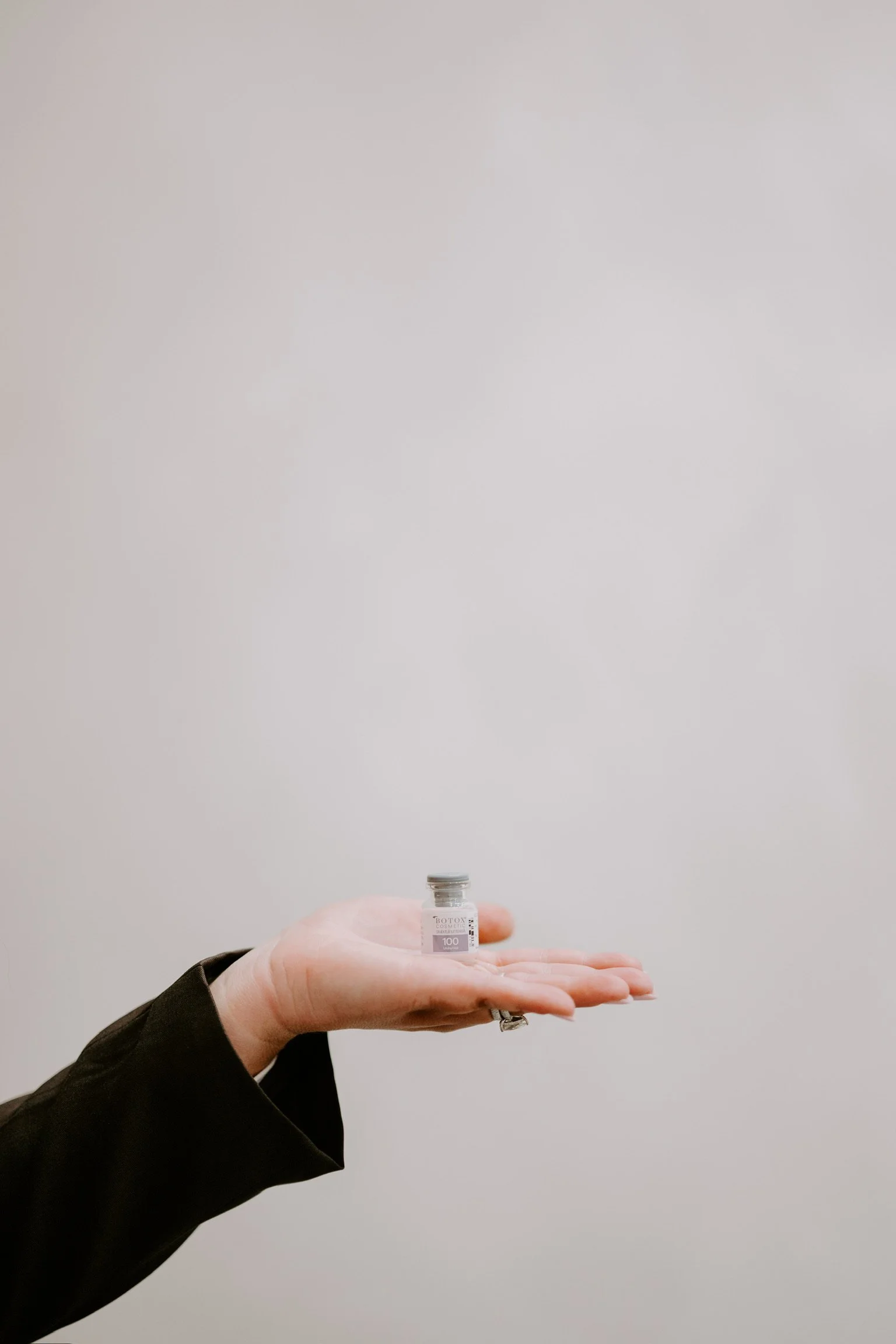 A hand holds a small vial labeled 'Botox' against a plain white background.