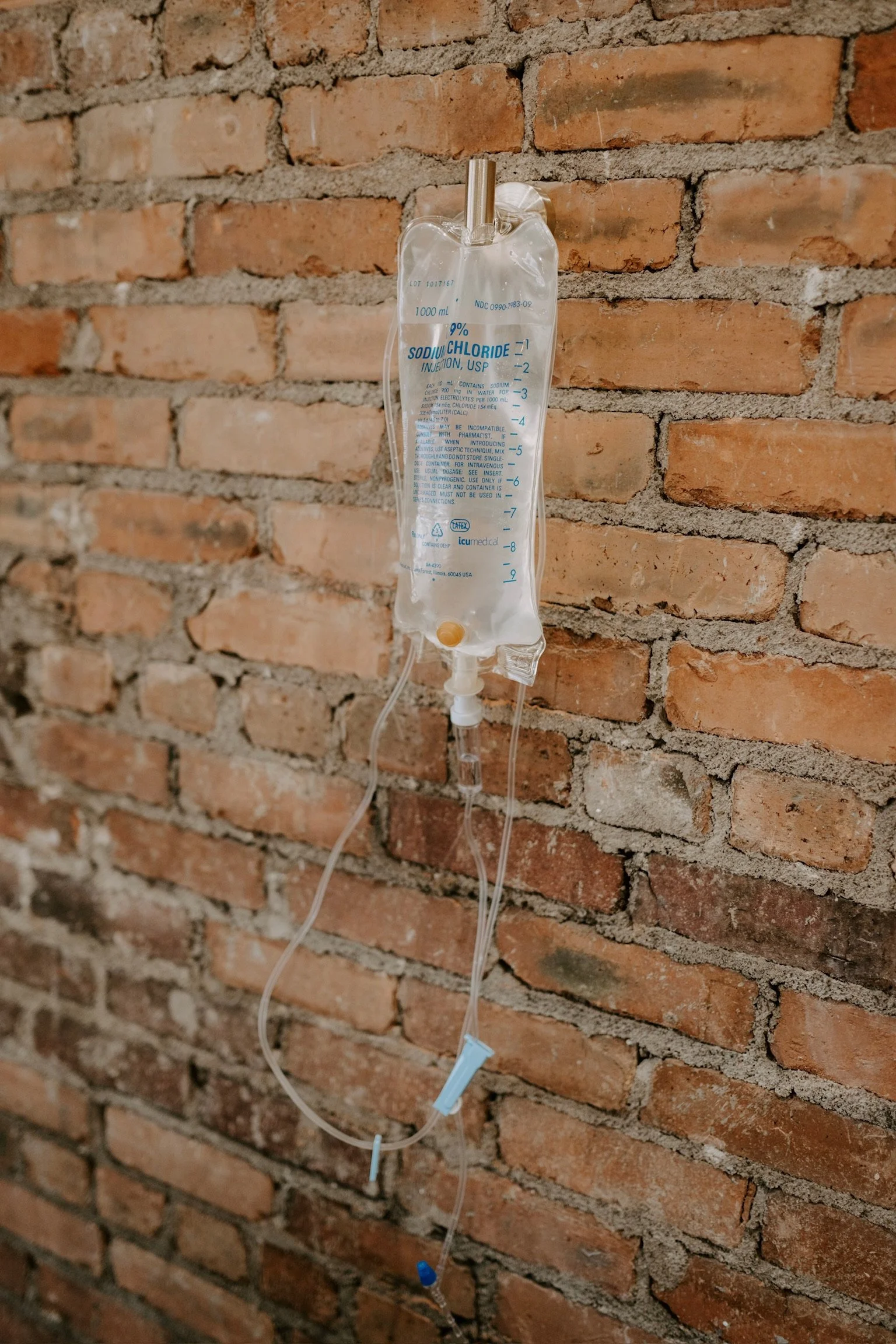 An intravenous (IV) hydration drip bag hanging on a hook against a brick wall.