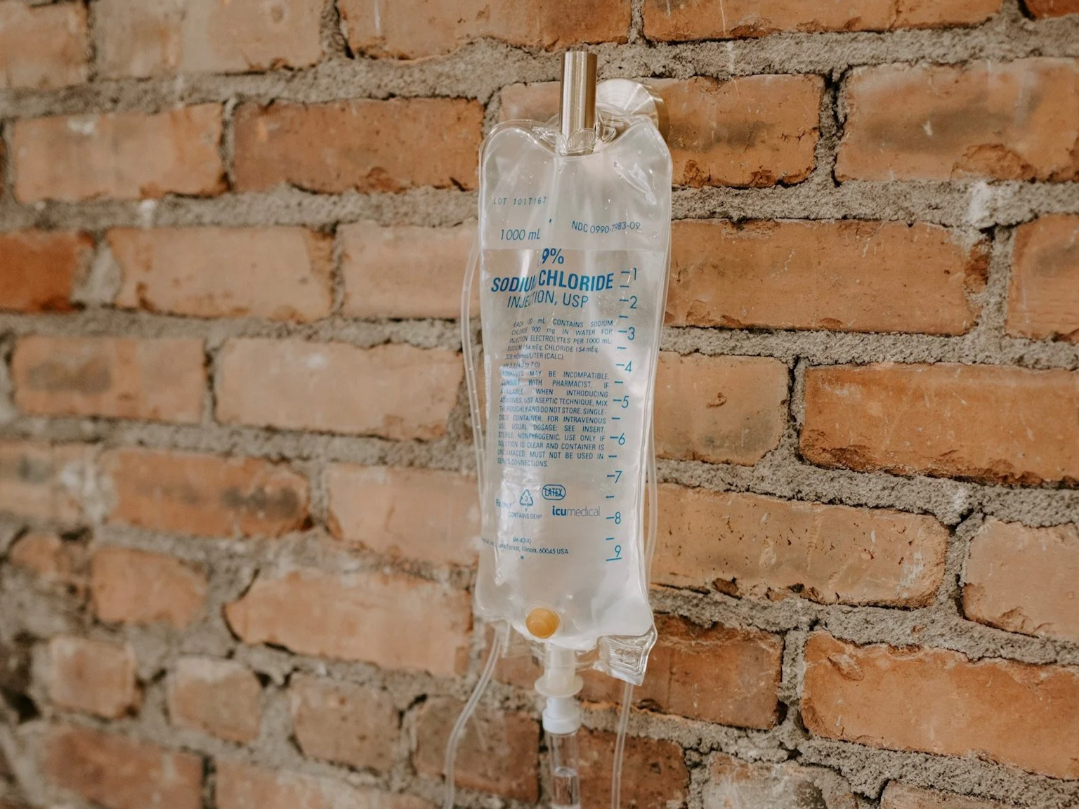 An intravenous (IV) bag labeled 'Sodium Chloride 0.9%' hanging on a brick wall.