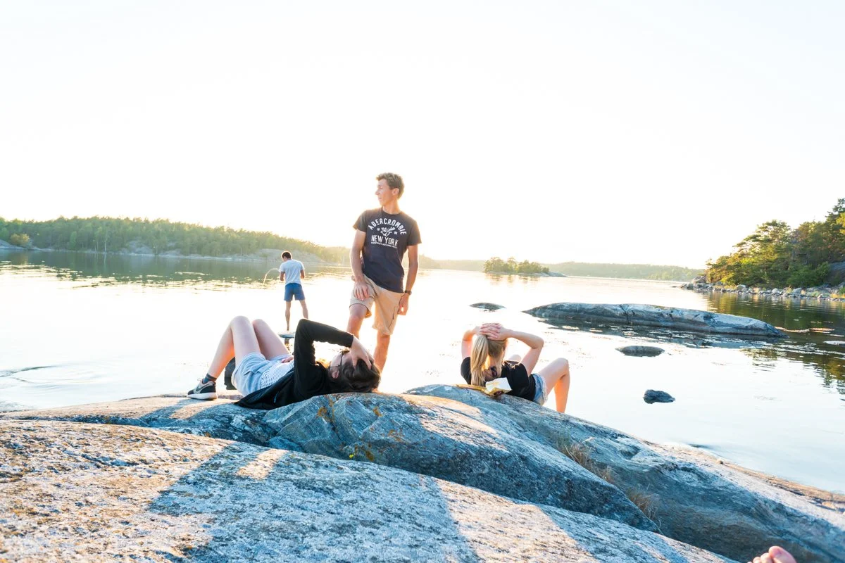 People relaxing on rocks by a river during sunset with trees in the background.