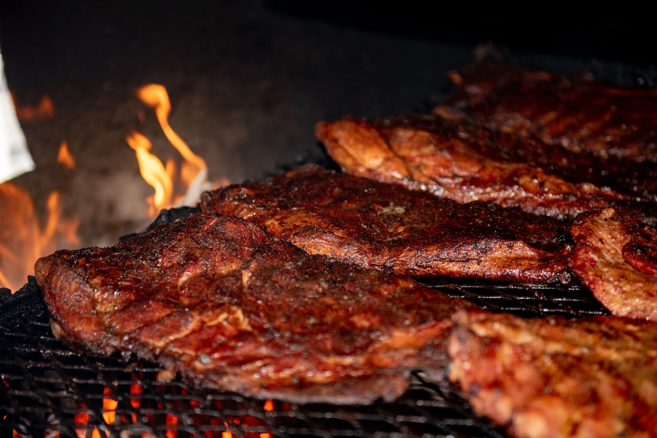 Close-up of meat grilling on a barbecue with visible flames and smoke.