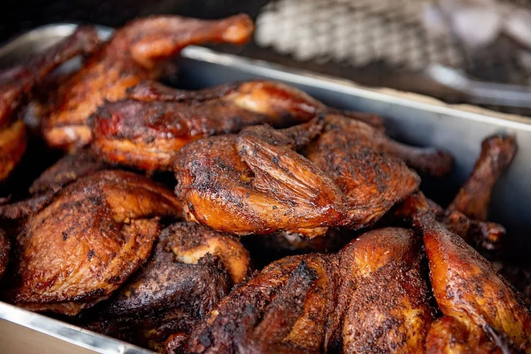 Close-up of grilled or smoked chicken with a dark, seasoned, crispy exterior in a serving tray.