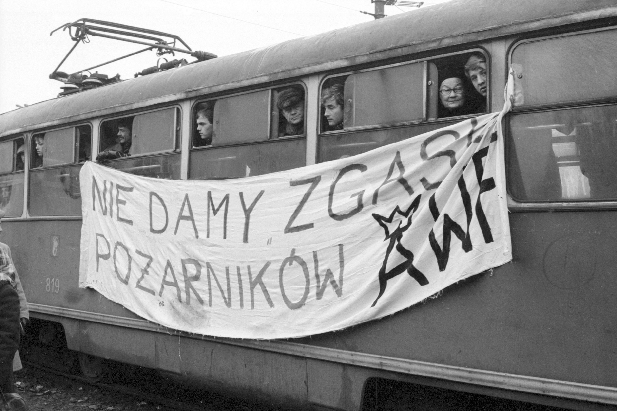 People on a trolley holding a banner with Polish writing during a protest or demonstration.