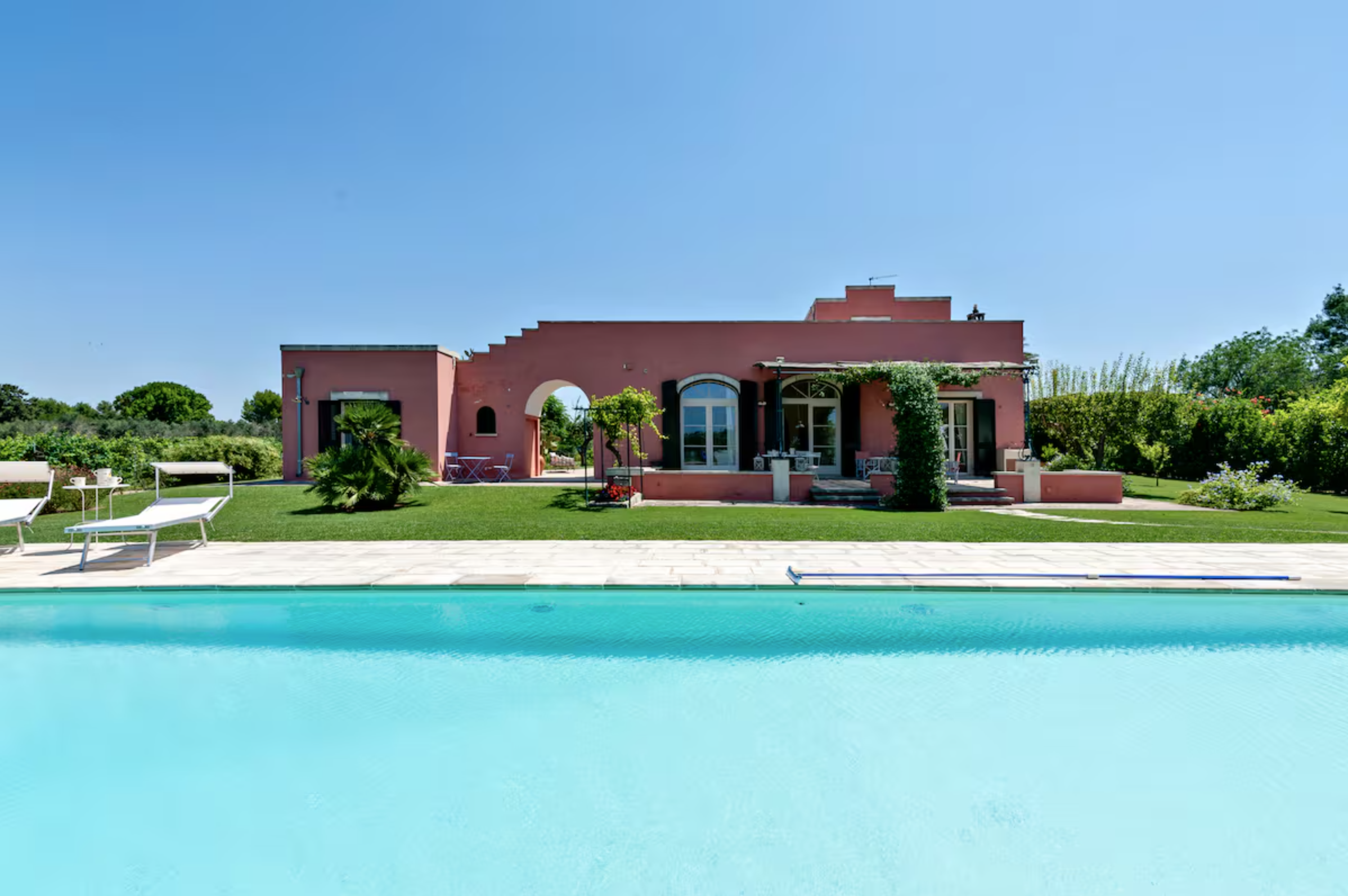 Ein rotes Haus mit Garten und Pool unter blauem Himmel.