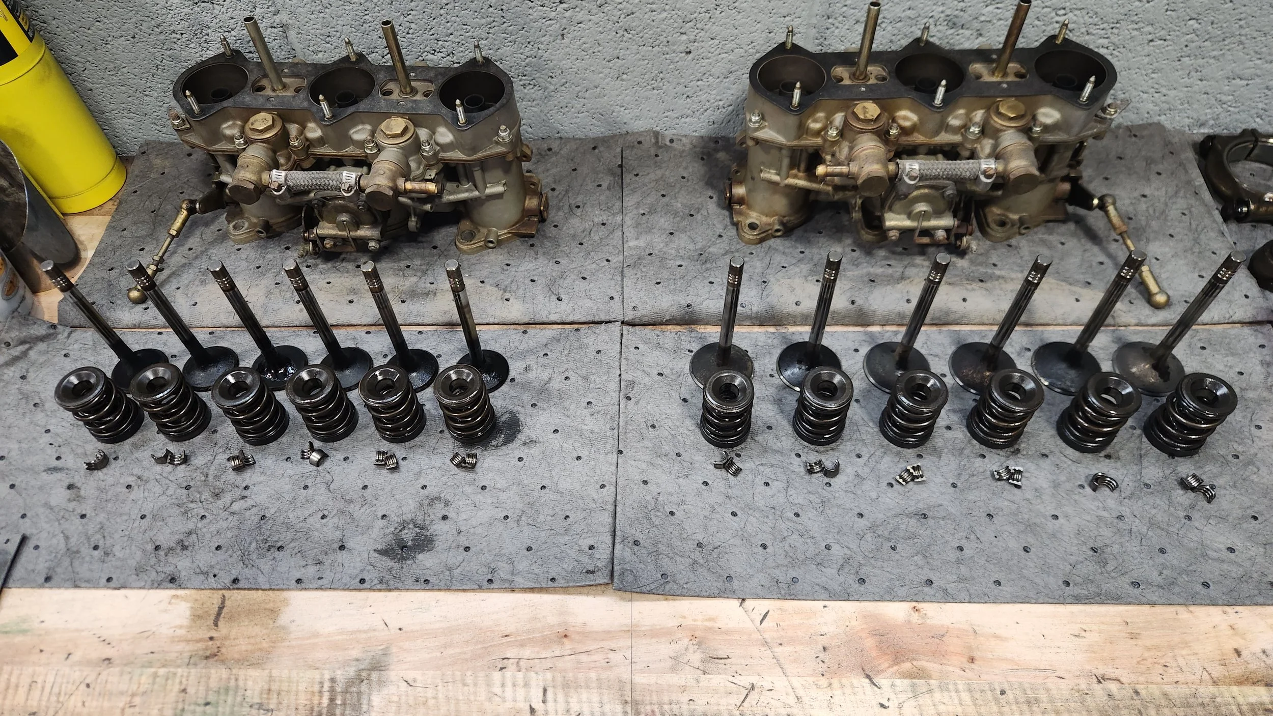 Car engine disassembled components including two Solex Carburators, valves, springs, and other parts laid out on workbenches.