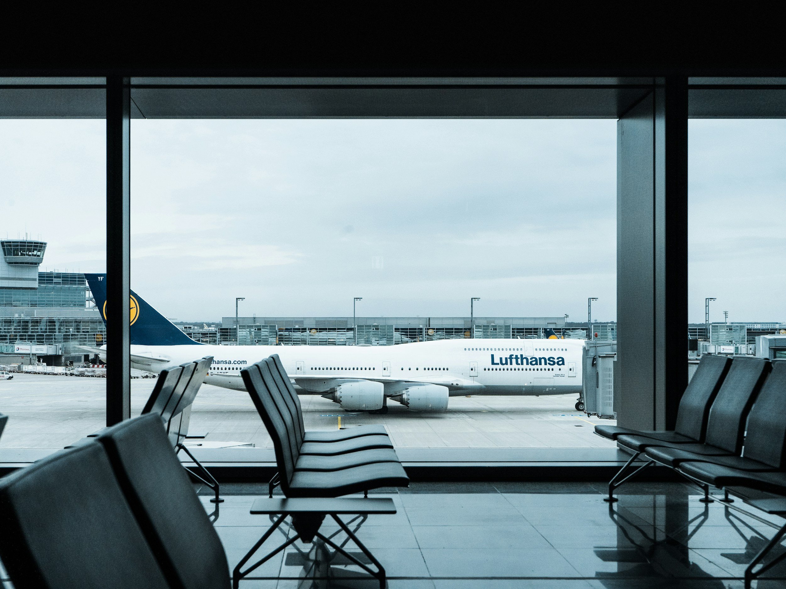 Empty seats inside an airport terminal with a view of a Lufthansa airplane parked at the gate through large windows.